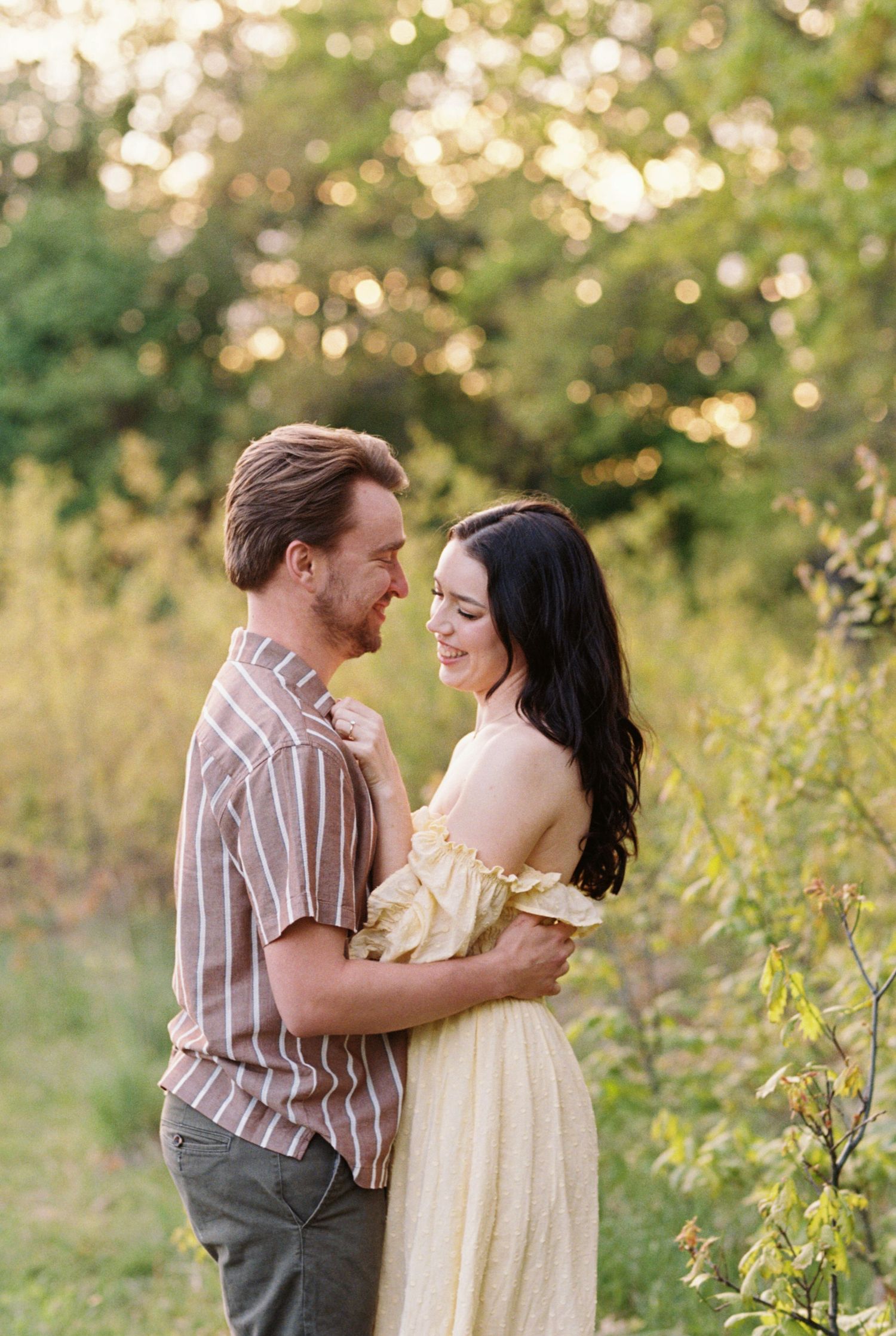 Romantic outdoor couple portrait in a meadow at golden hour with soft bokeh and wildflowers in the background.
