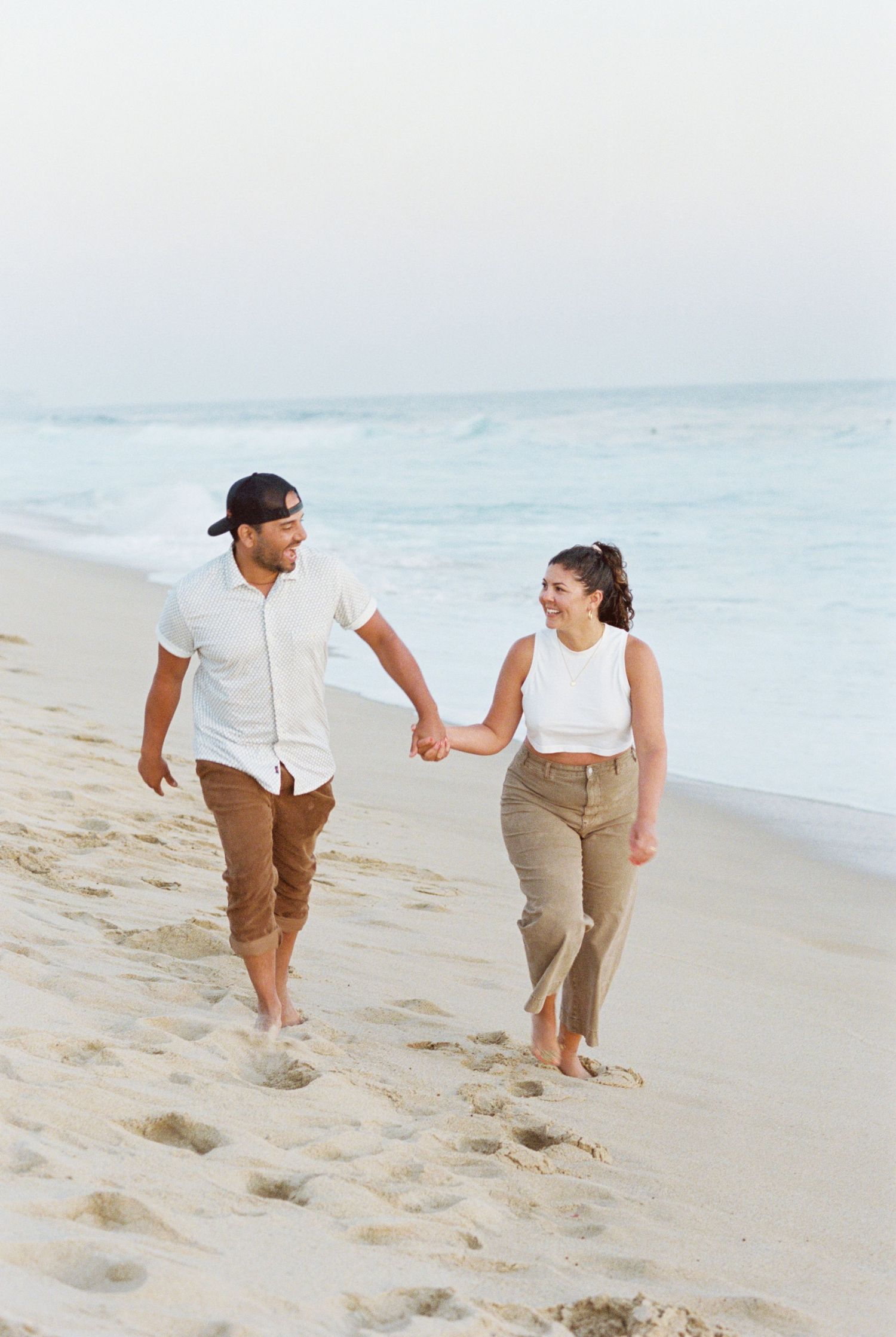 A couple walking hand in hand on a sunset Mexico beach wearing casual clothes and enjoying a romantic stroll. Kirstie Whitaker Photography