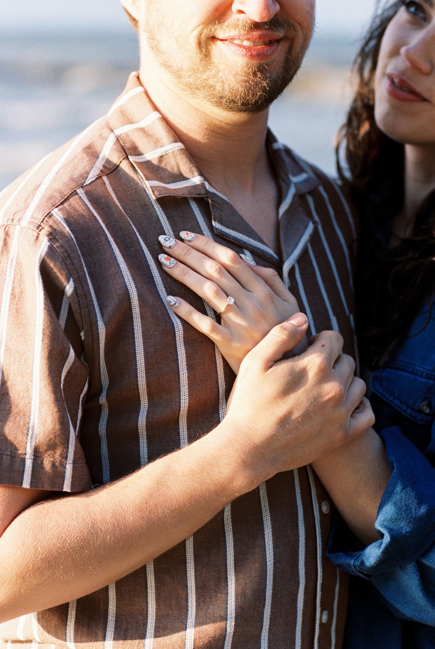 Close-up shot of hands lovingly embracing while wearing a brown striped shirt and blue top in warm sunlight.