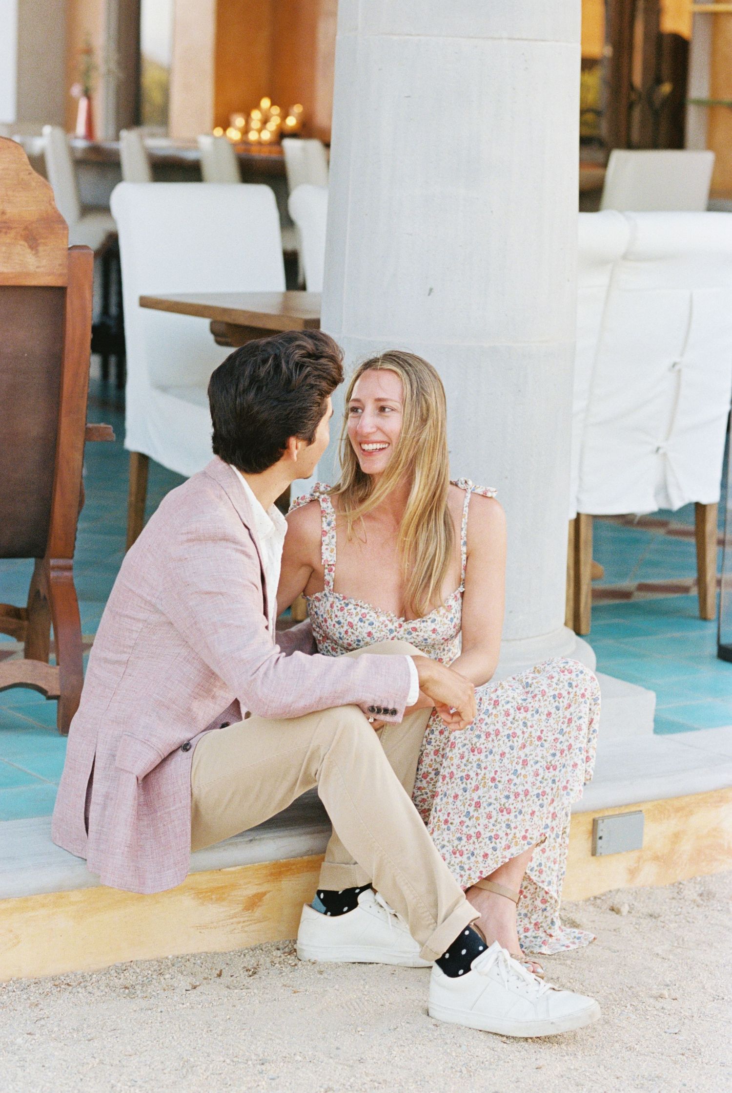 A couple in casual spring attire sharing a sweet moment on a patio with turquoise accents and white pillars.