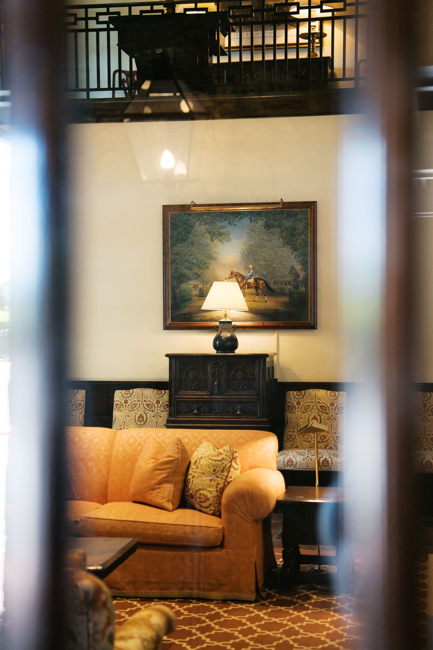 A cozy living room interior with a peach sofa, framed artwork, and table lamp viewed through decorative metal railings.