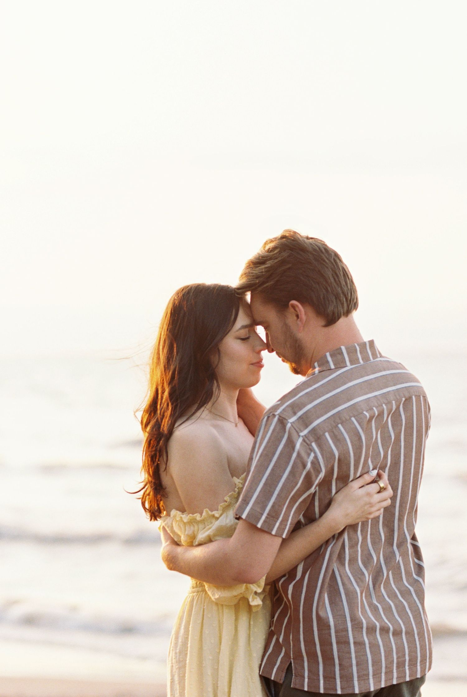 A romantic couple embraces on a sunlit beach during golden hour, creating a dreamy silhouette against the ocean backdrop.