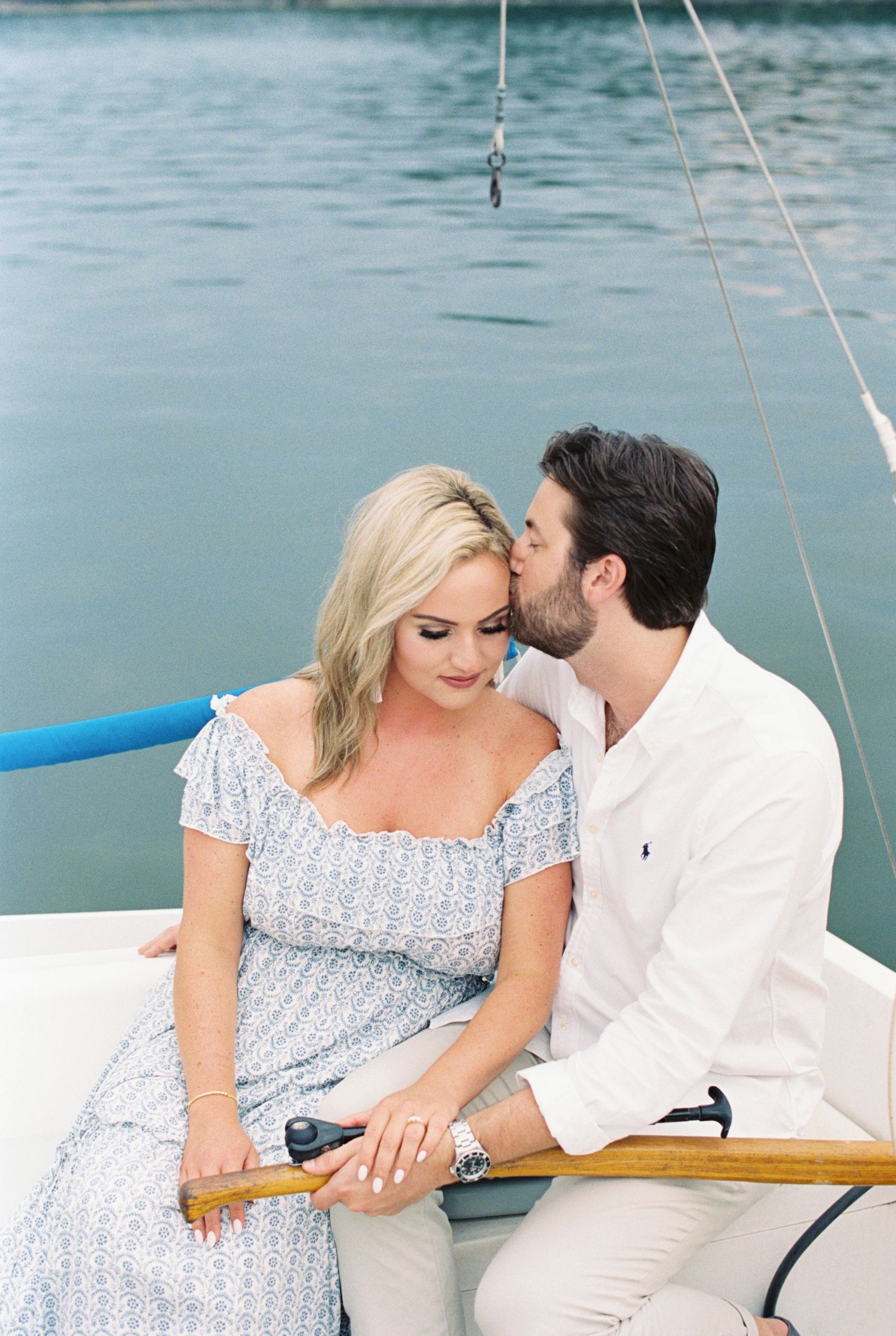 Romantic couple sharing a tender moment while sitting together on a sailboat on calm blue waters.
