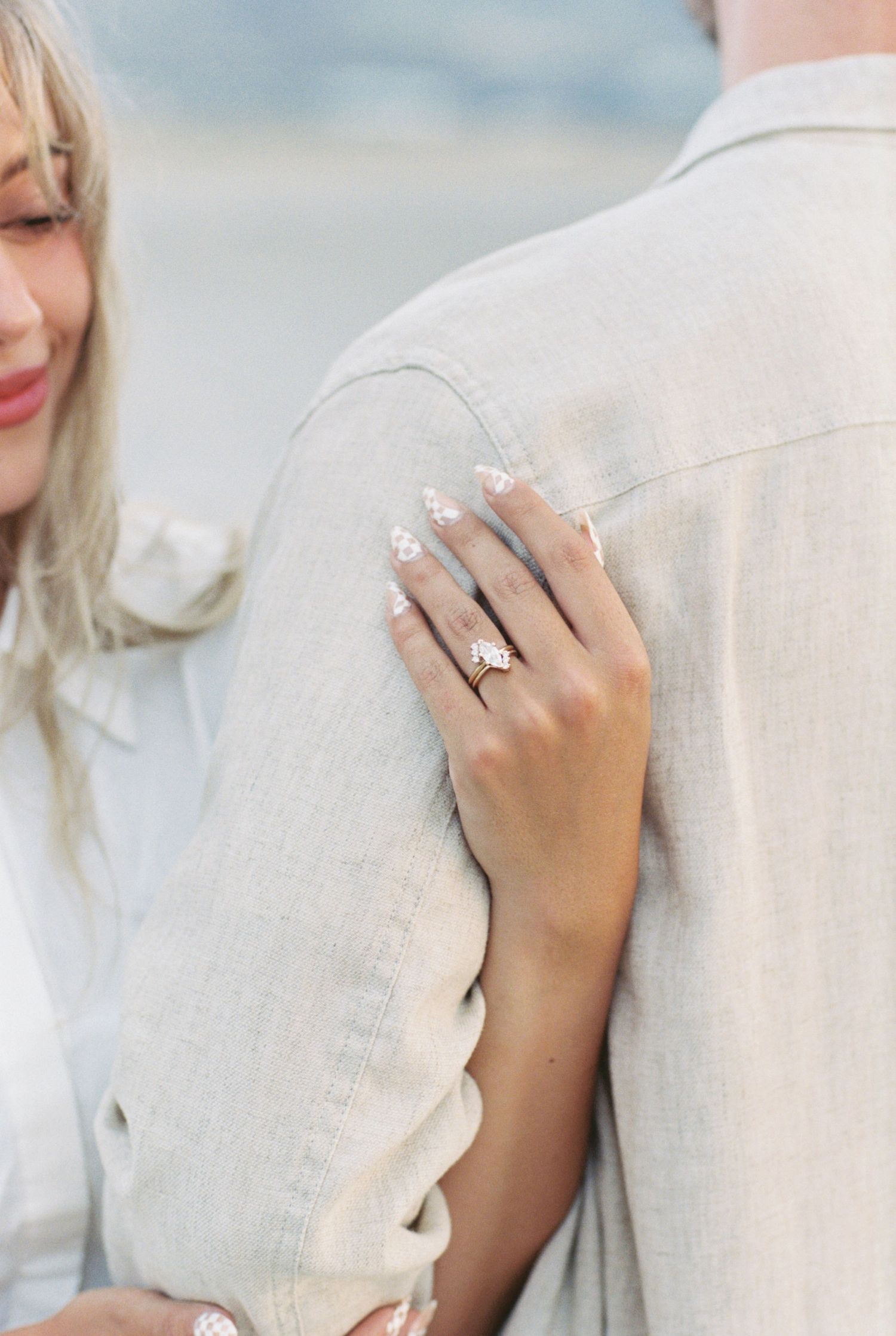 Close up of an engagement ring shown on hand resting against light colored clothing during a romantic moment.