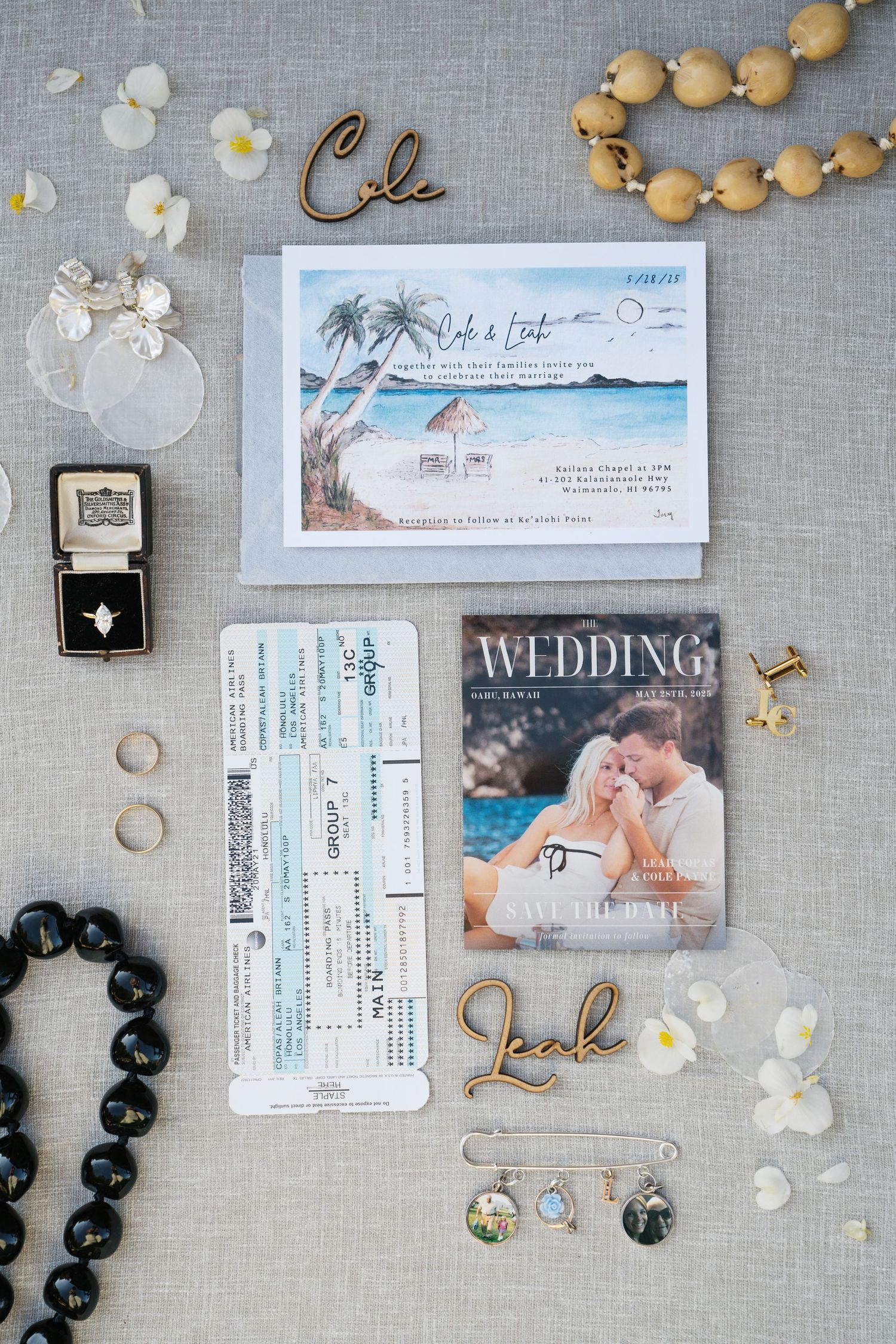 Wedding planning flatlay with invitation cards, beaded necklaces, and scattered flower petals on a gray linen background.