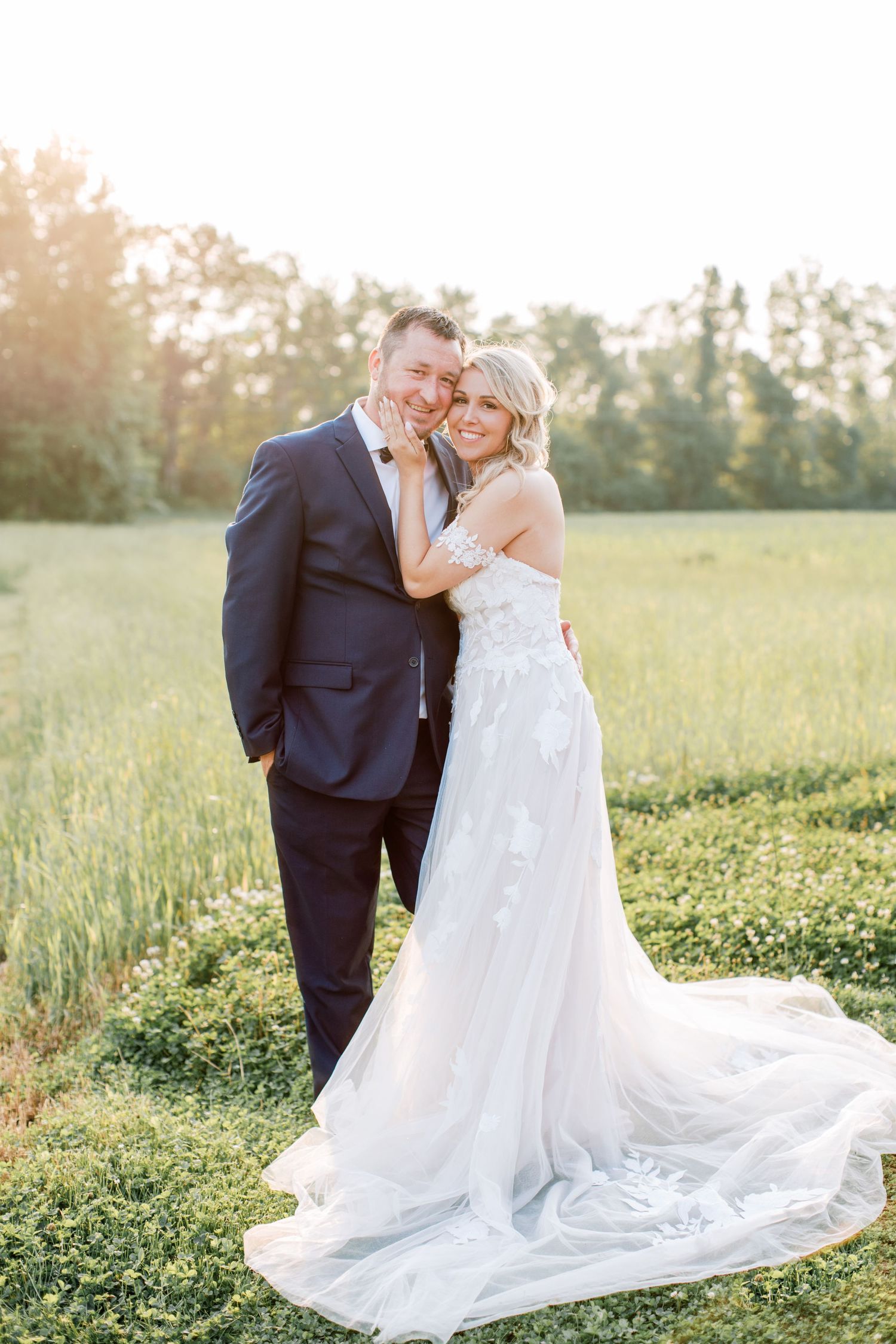 A romantic sunset wedding portrait of a couple in formal attire standing in a meadow. Kirstie Whitaker Photography