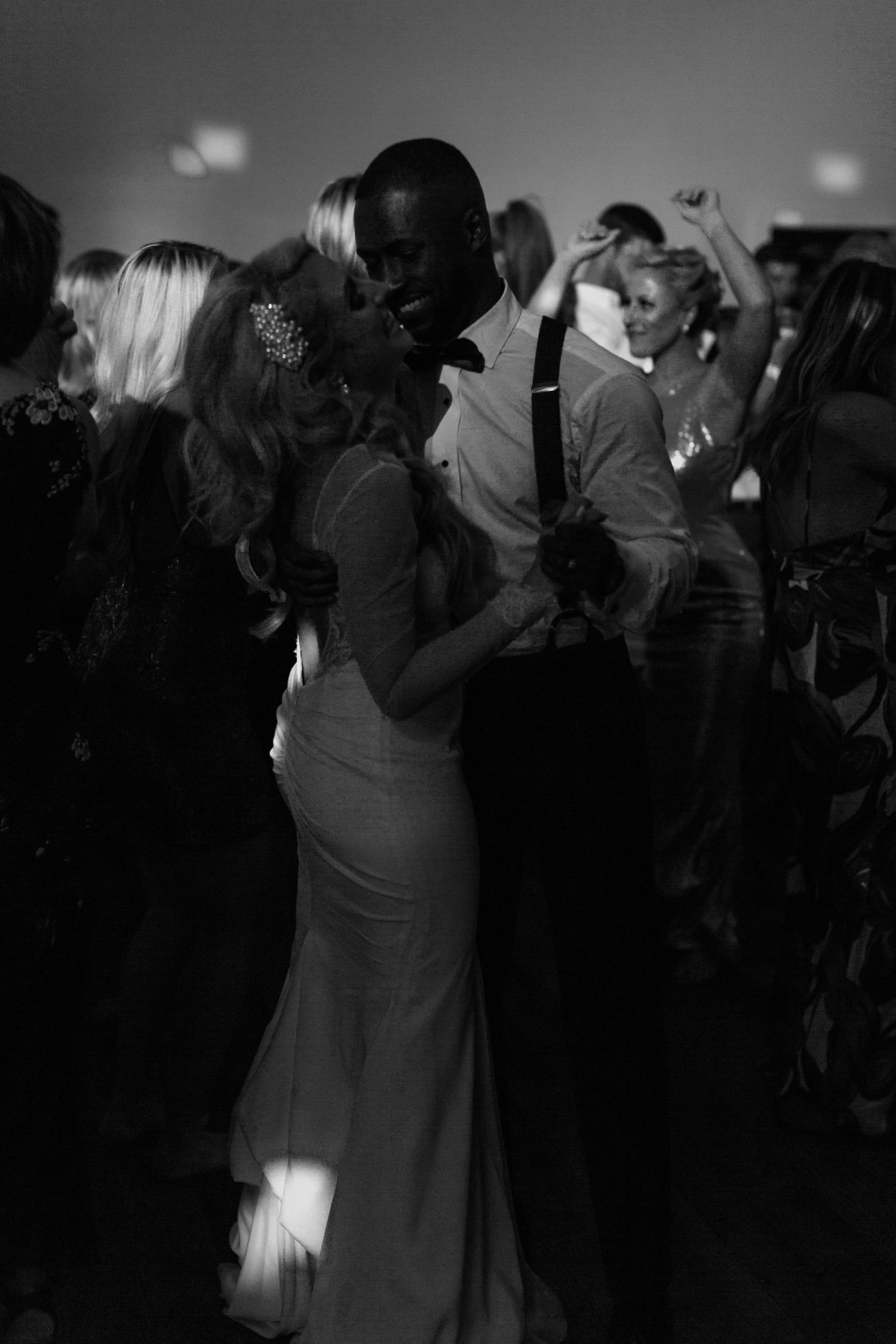 Monochrome photo of a couple dancing intimately at an elegant event surrounded by other dancers in a dark room.