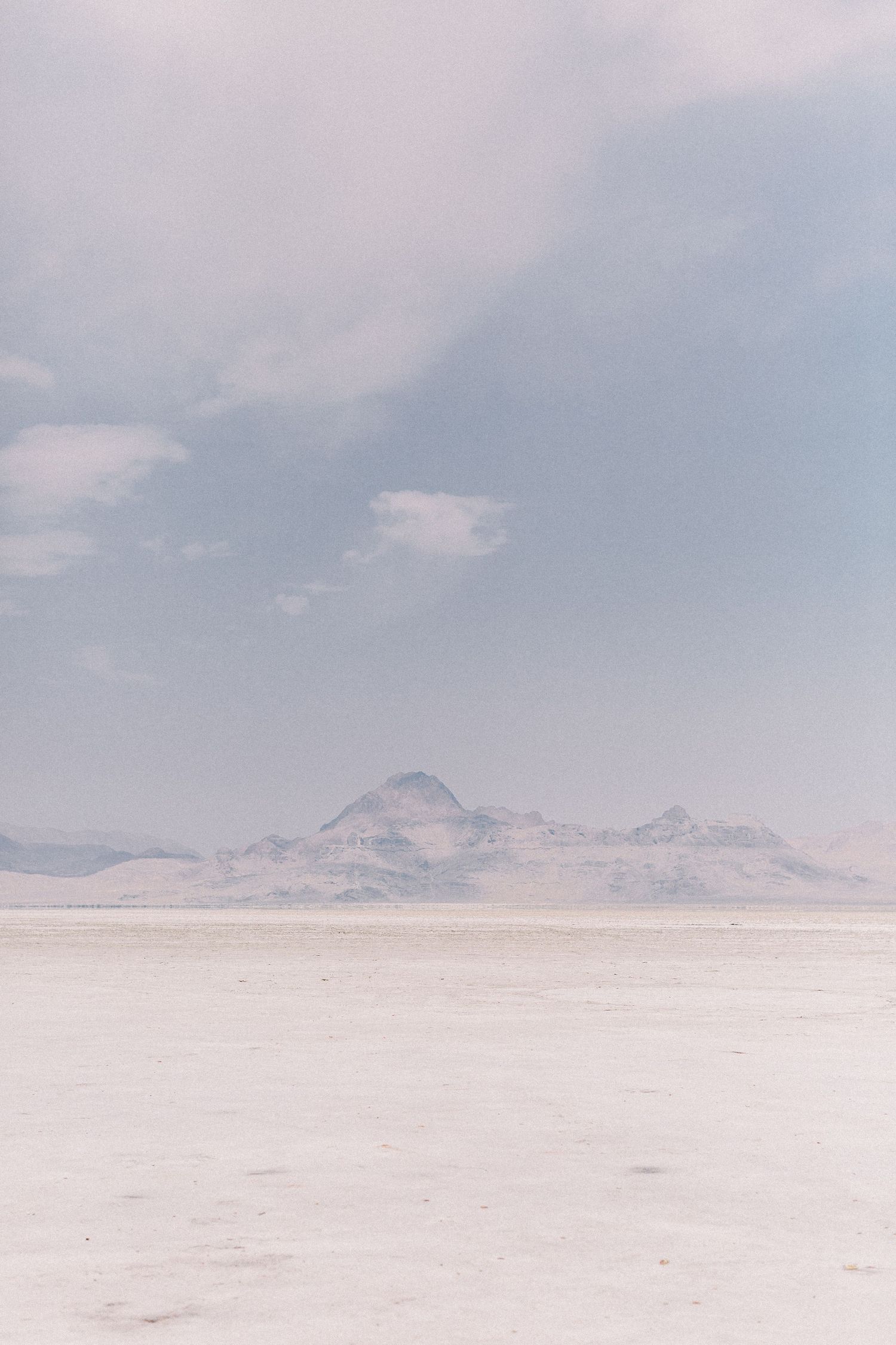 A serene desert landscape with distant purple mountains rising above the stark white salt flats under a pale cloudy sky. Kirstie Whitaker