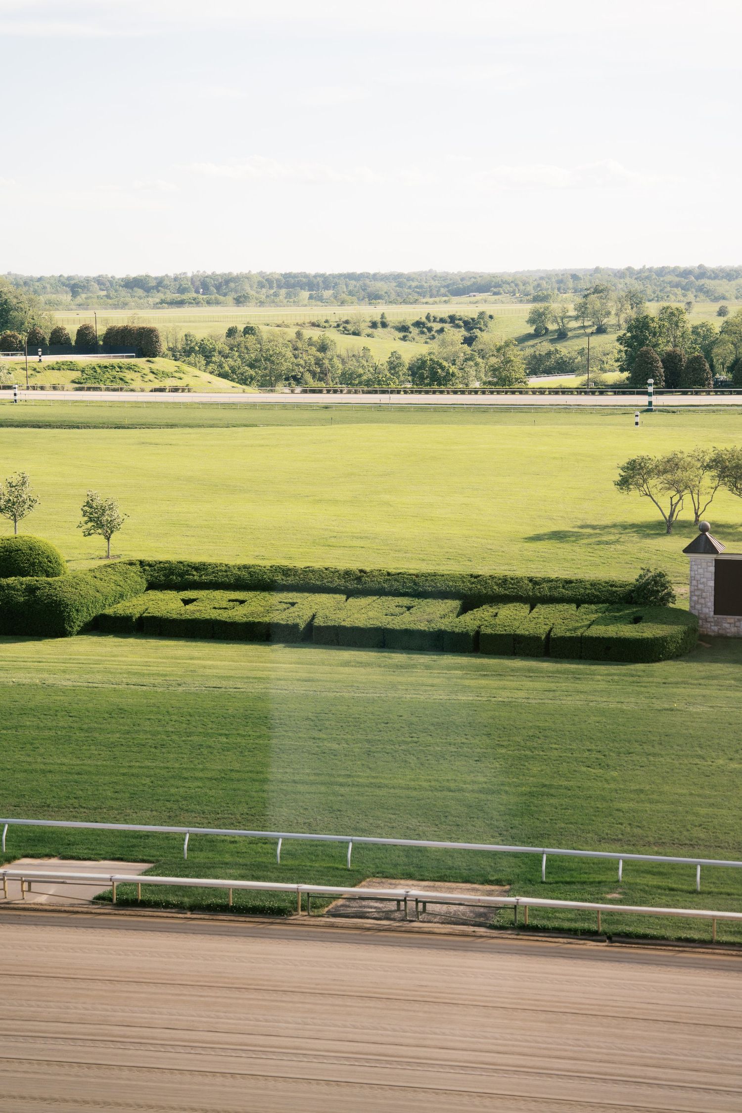 Rolling green hills and manicured grass fields with white fencing viewed from an elevated wooden deck on a sunny day.