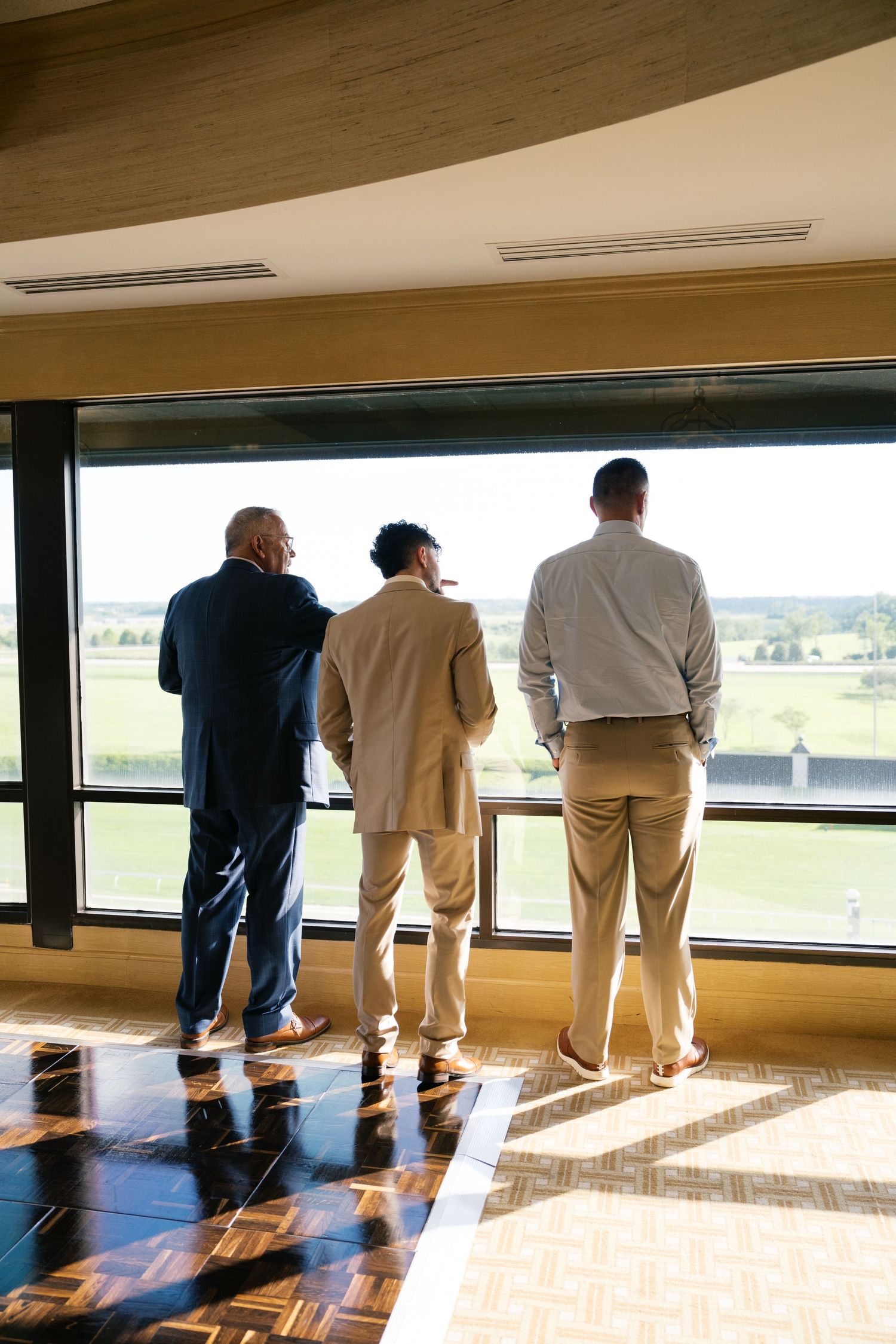 Three people stand together looking out through large windows at a scenic landscape view from an elegant interior space.