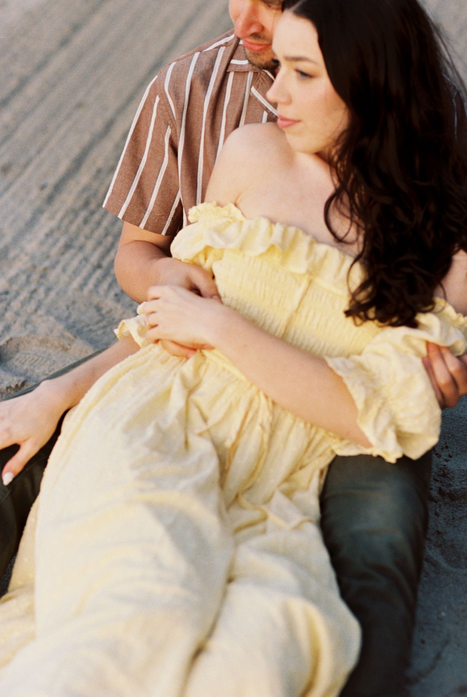A romantic moment captured on wooden flooring with a person wearing a yellow ruffled sundress and another in a striped shirt.