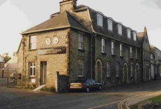 Historic stone building with dormer windows and parked car on quiet street corner in English town.