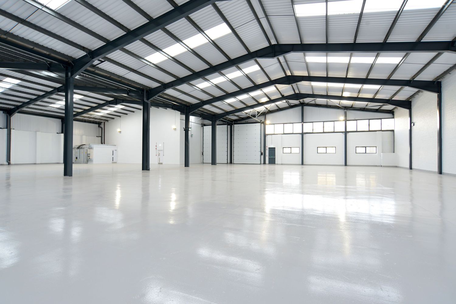 Empty modern warehouse interior with polished white epoxy floor, steel frame structure, and large windows.