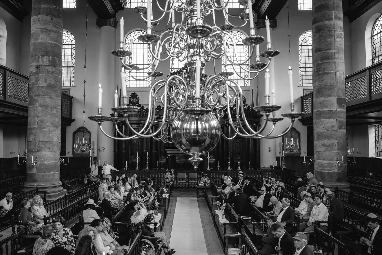 Black and white photo of church wedding ceremony with ornate chandelier and filled pews.