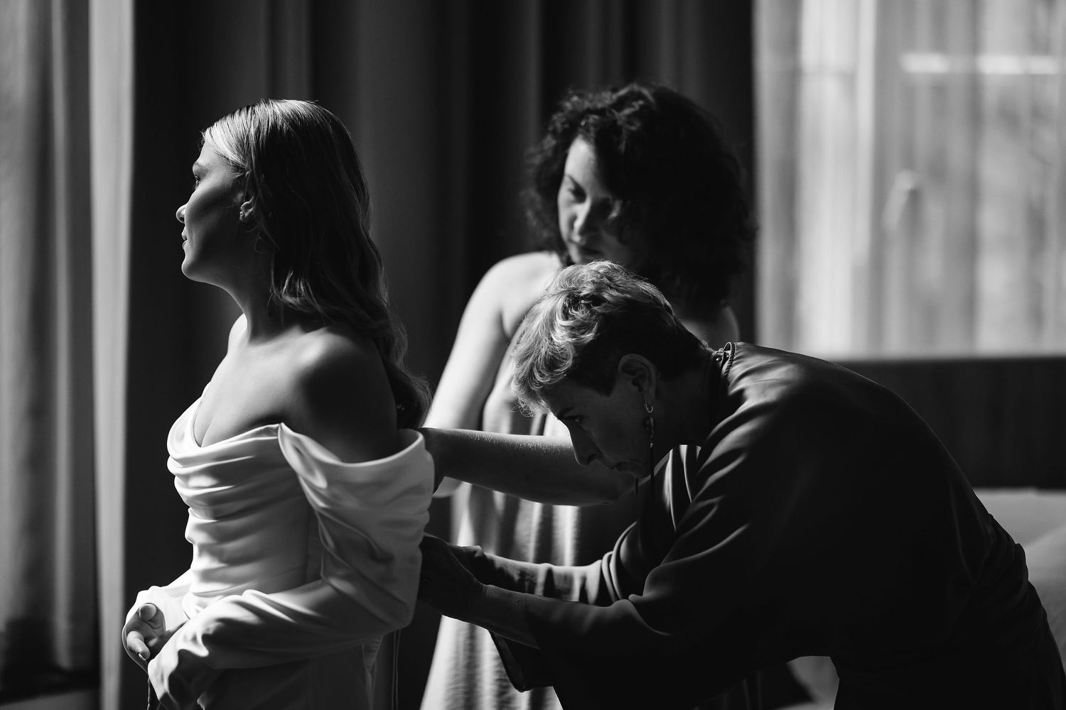 Intimate black and white photograph of wedding preparations in dramatic window light.