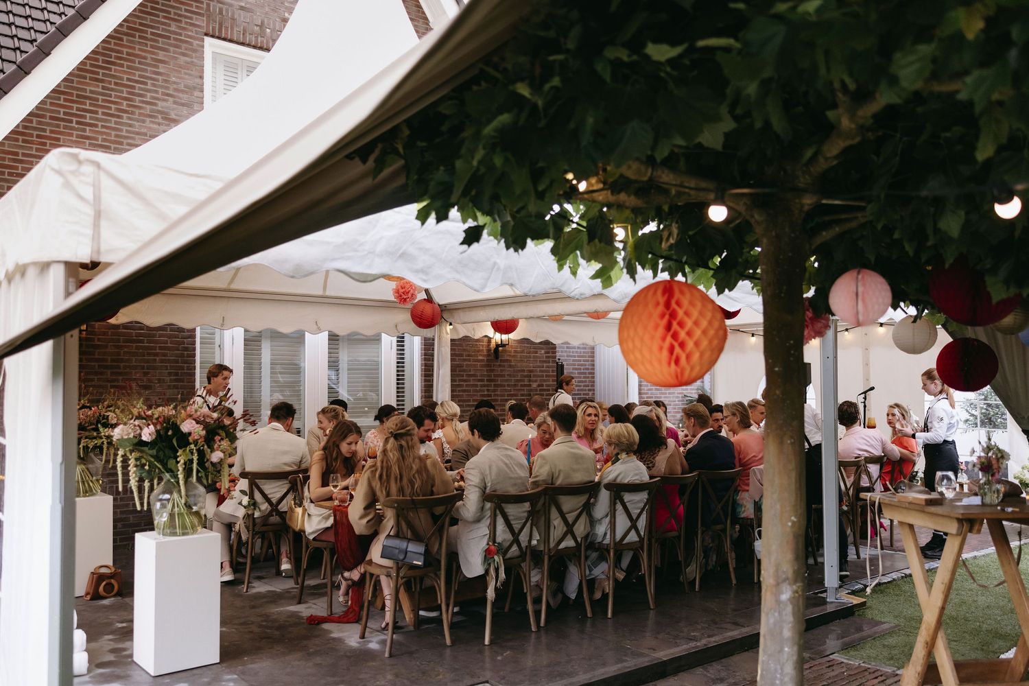 Wedding reception setup under outdoor tent with festive paper lantern decorations.