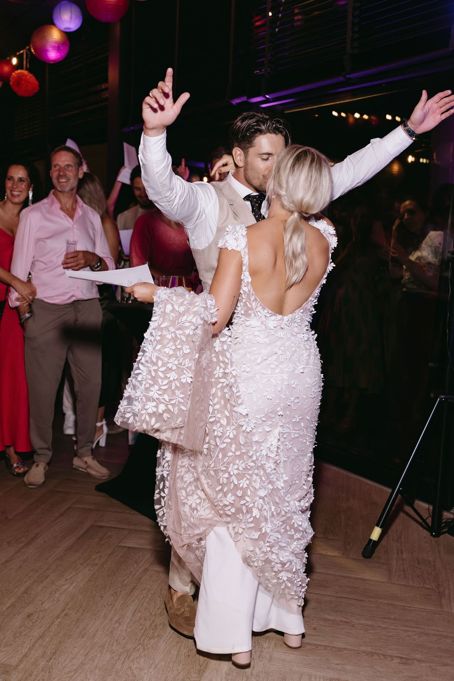 Dancing celebration at a wedding reception with colorful overhead lighting and decorations.