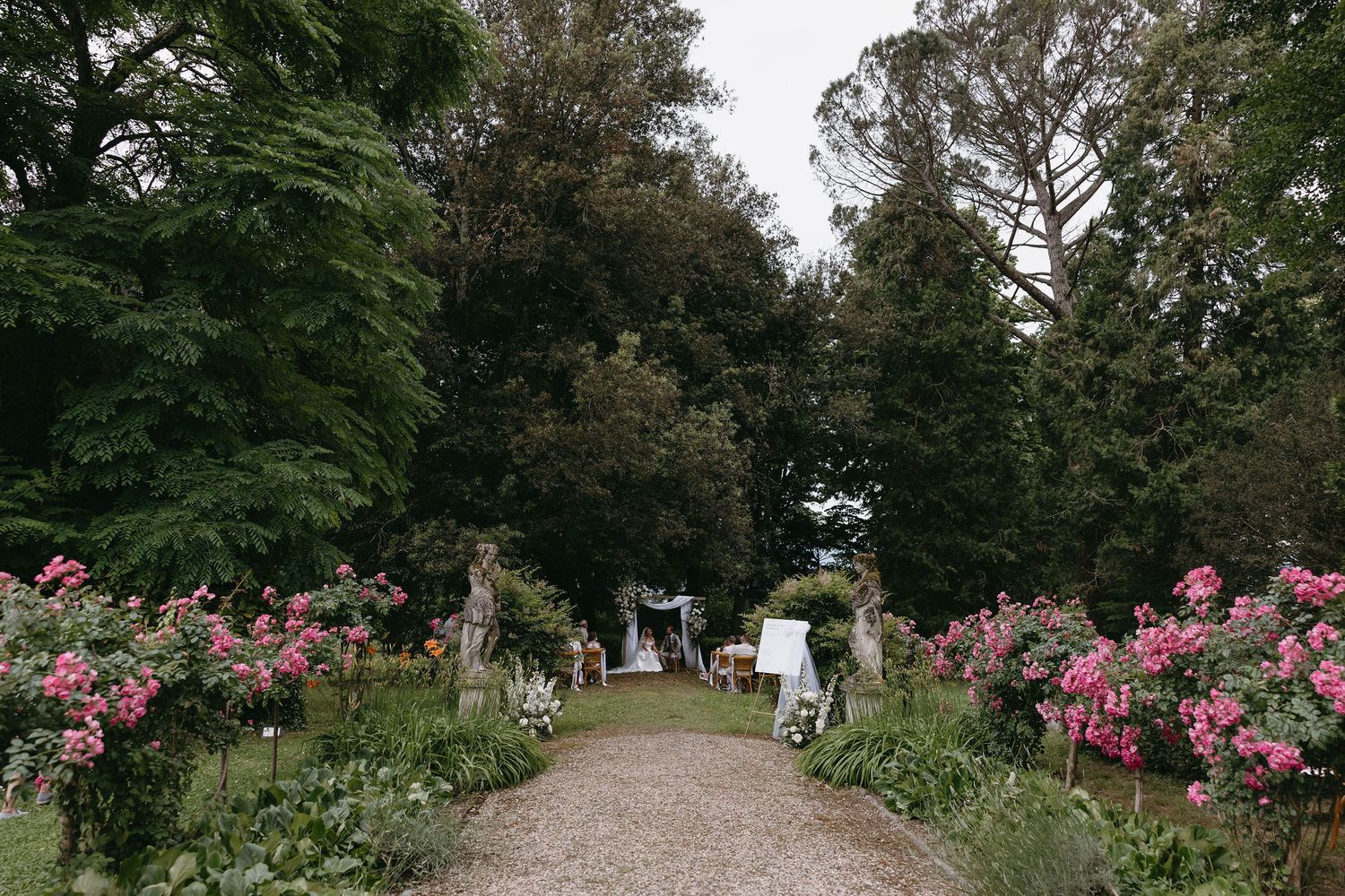 Garden pathway lined with blooming pink flowers leading to a wedding ceremony space.