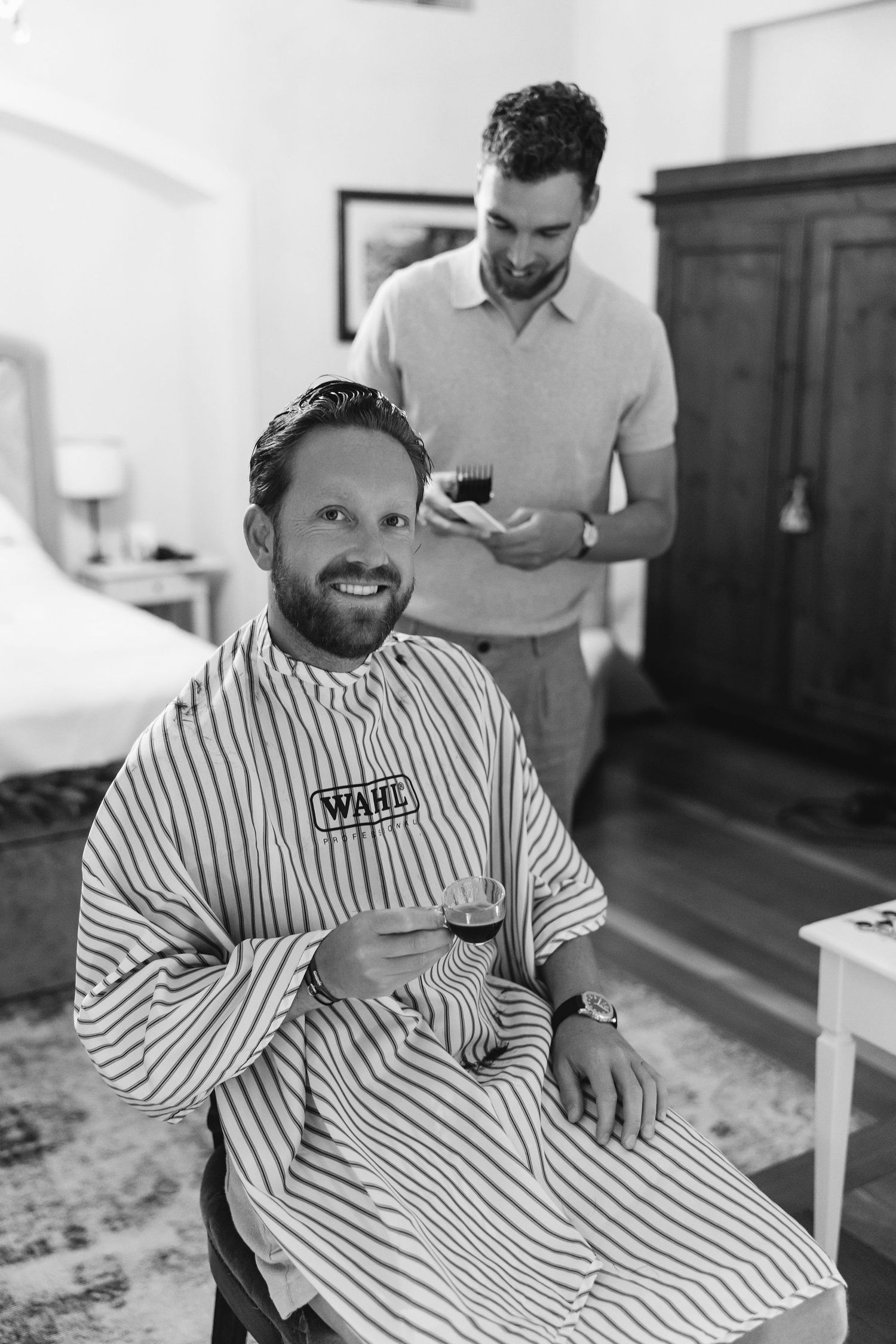 A candid moment during wedding preparations as someone gets a haircut in a striped barber cape.