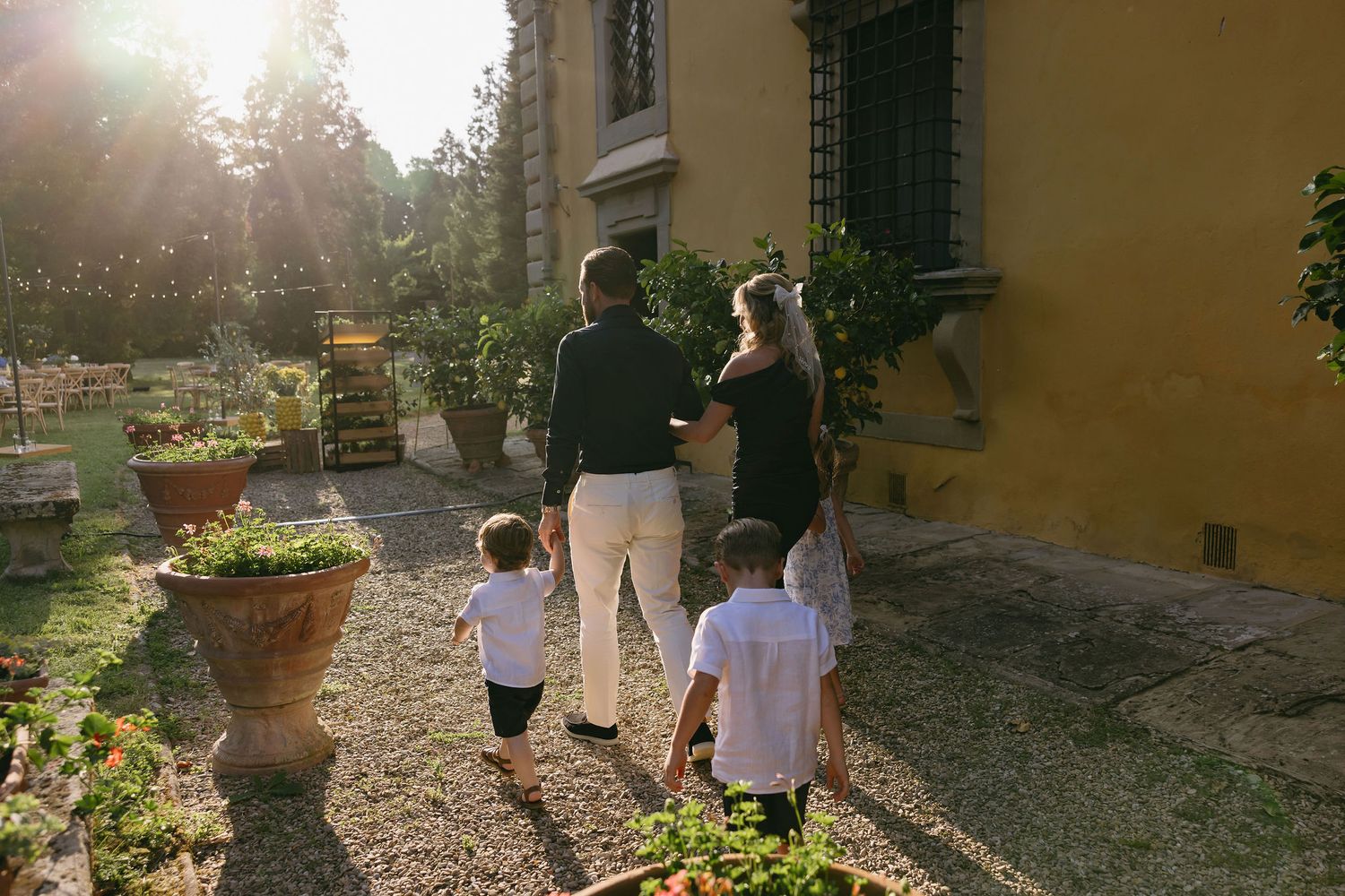 Wedding guests walking along a sun-drenched path by an Italian villa.
