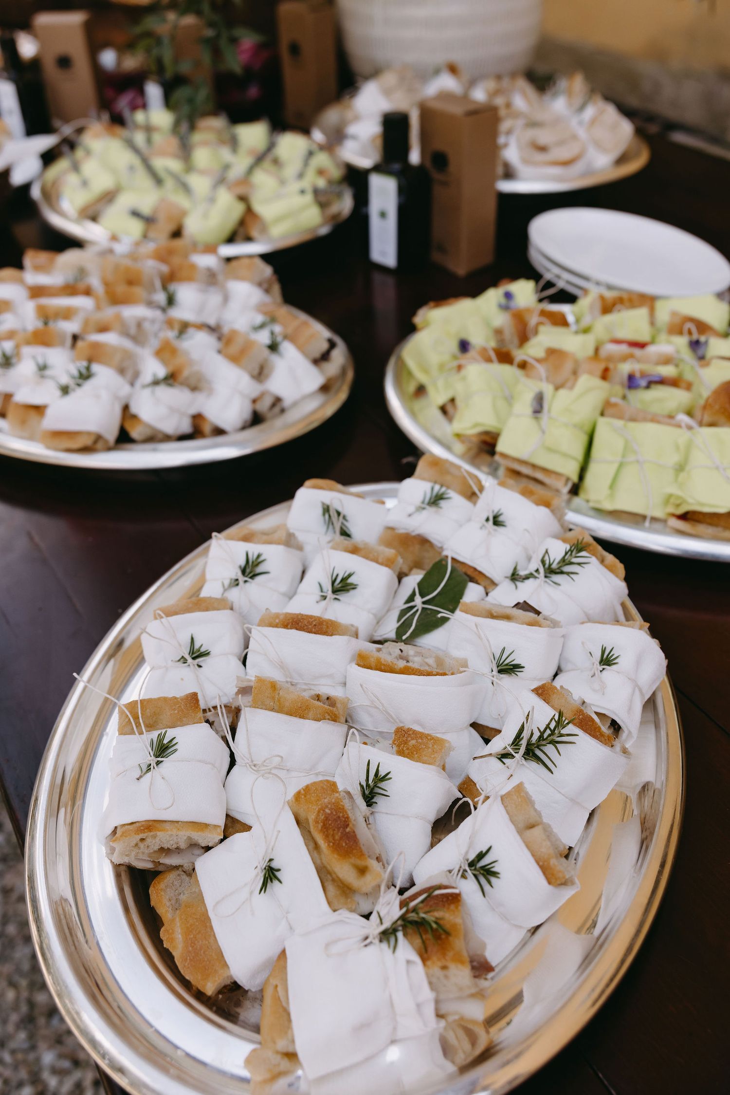 Catered sandwich platters garnished with herbs wrapped in white paper.