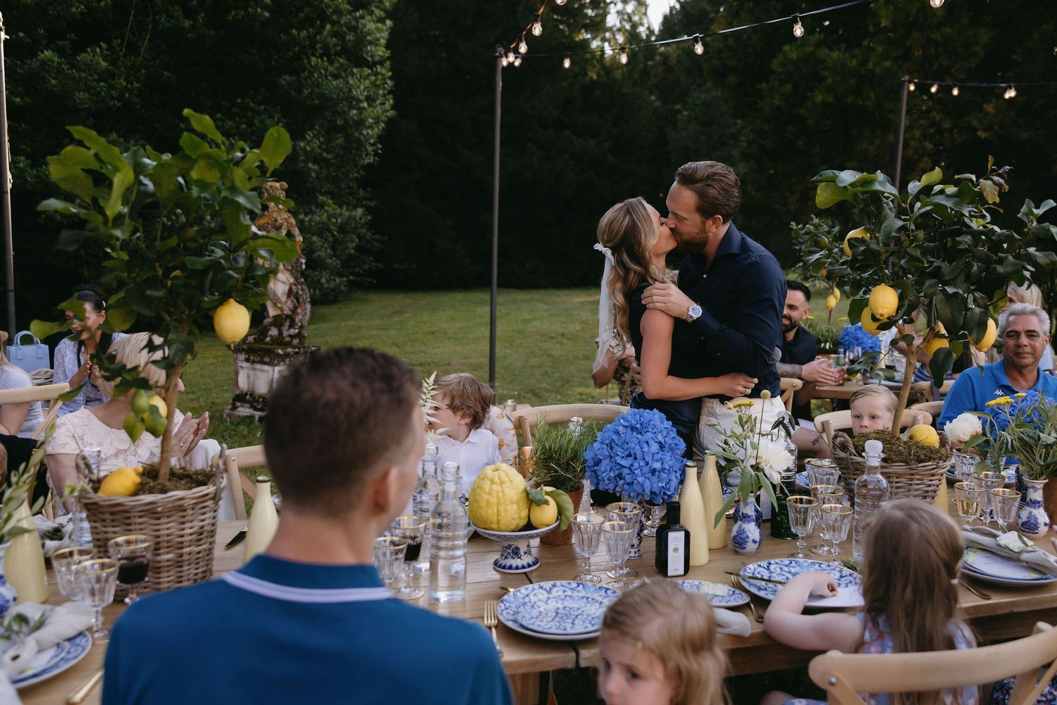 Outdoor wedding reception with decorated tables and string lights under trees.