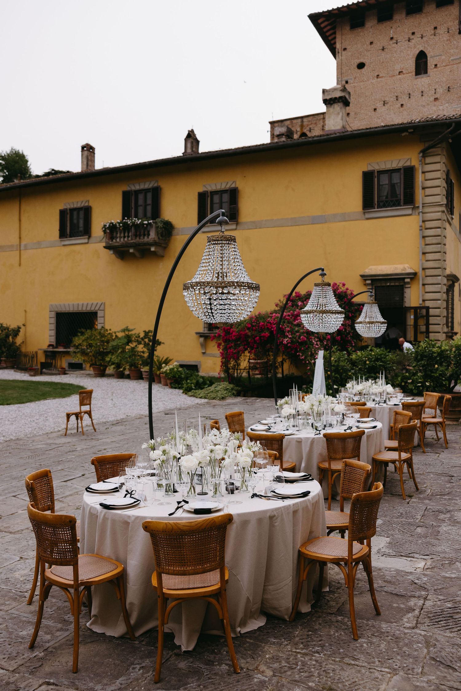 Outdoor wedding reception setup with crystal chandeliers and round tables at a rustic villa.