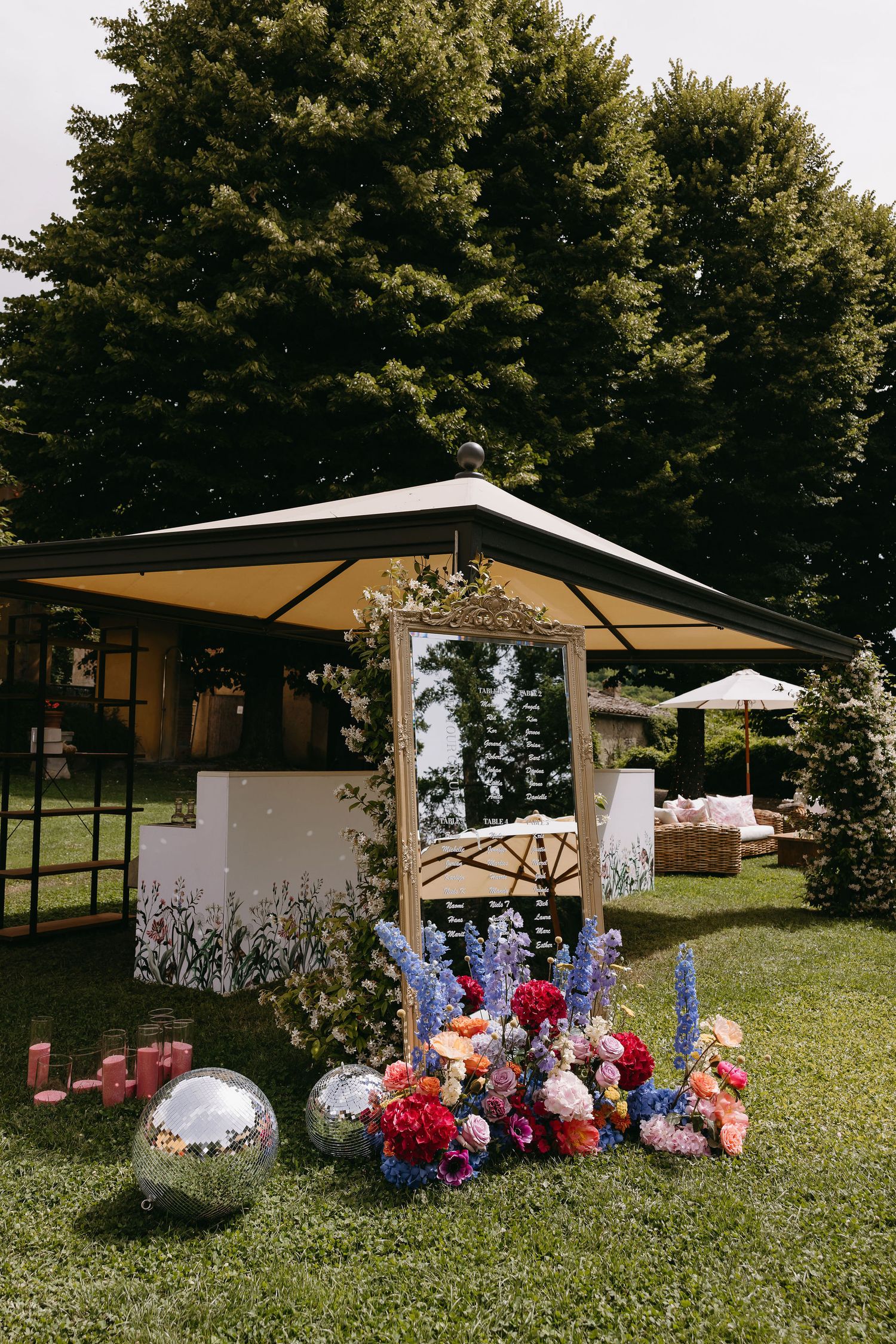 Outdoor wedding kiosk decorated with vibrant blue and pink floral arrangements against a backdrop of green trees.