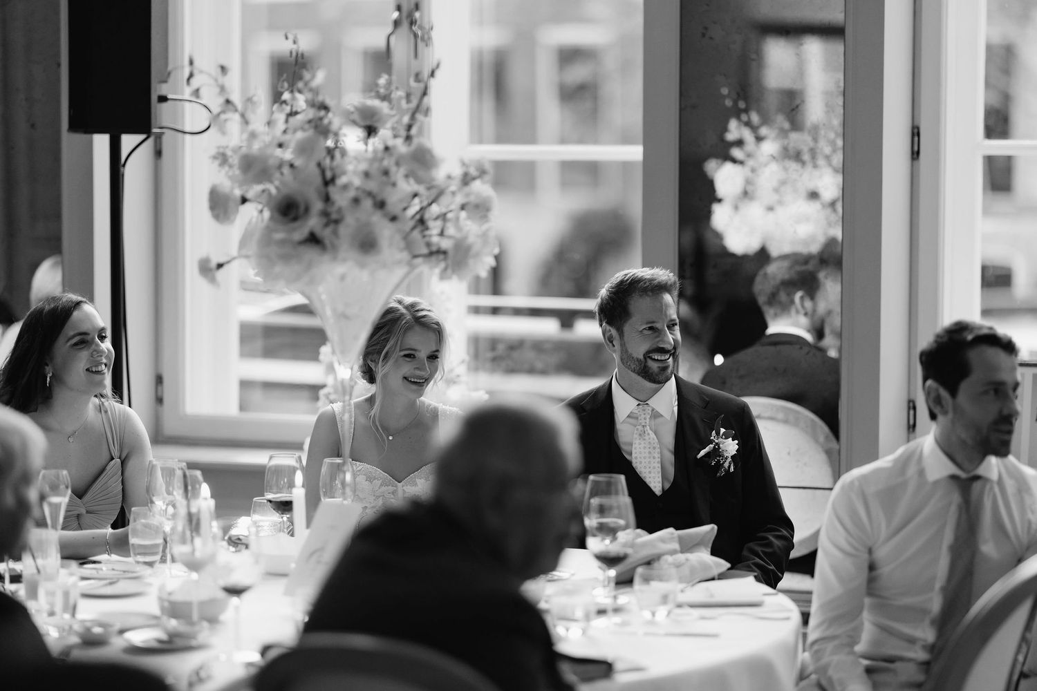 Black and white photo of wedding guests laughing during reception dinner.