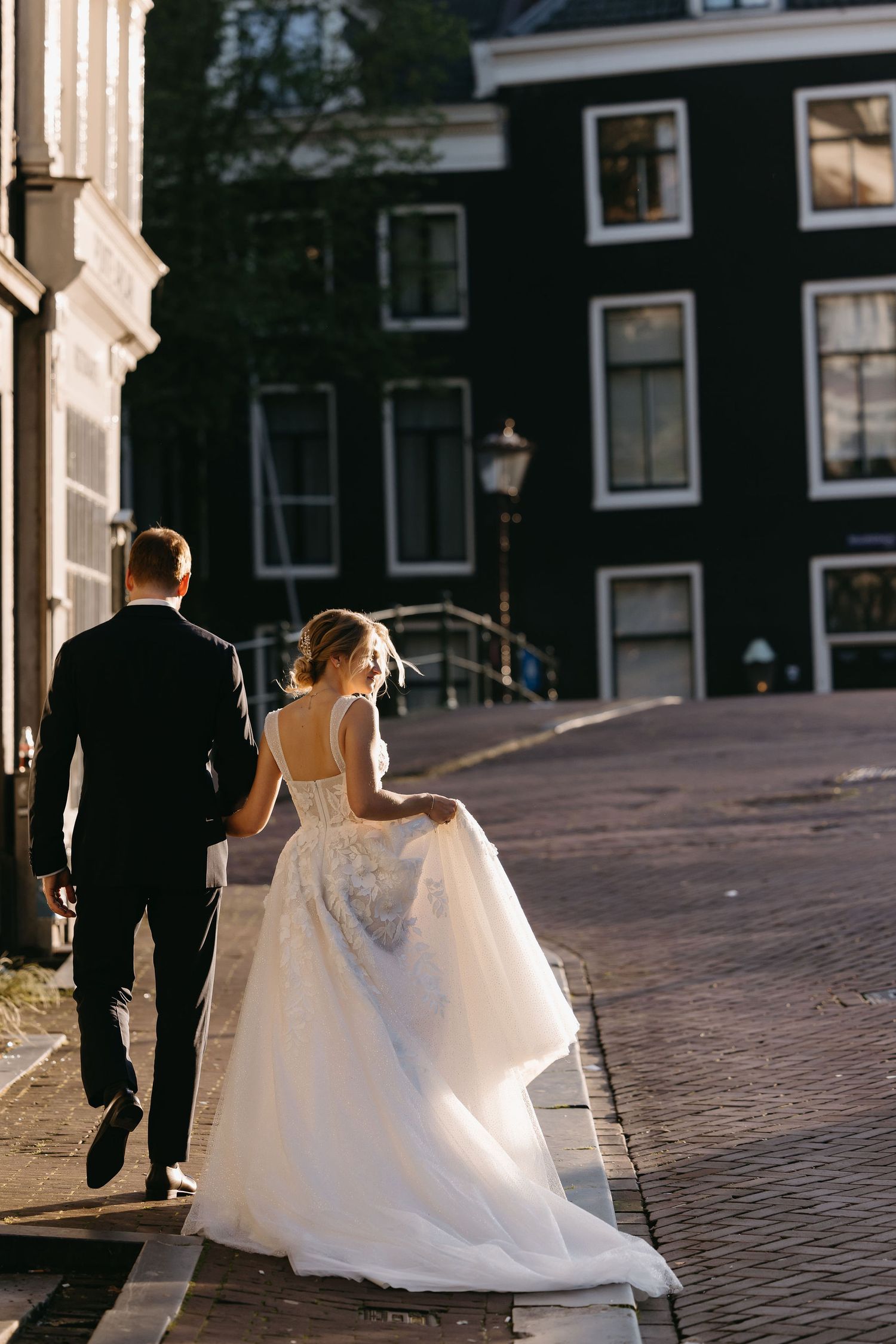 Newlyweds walking along a cobblestone street during golden hour.