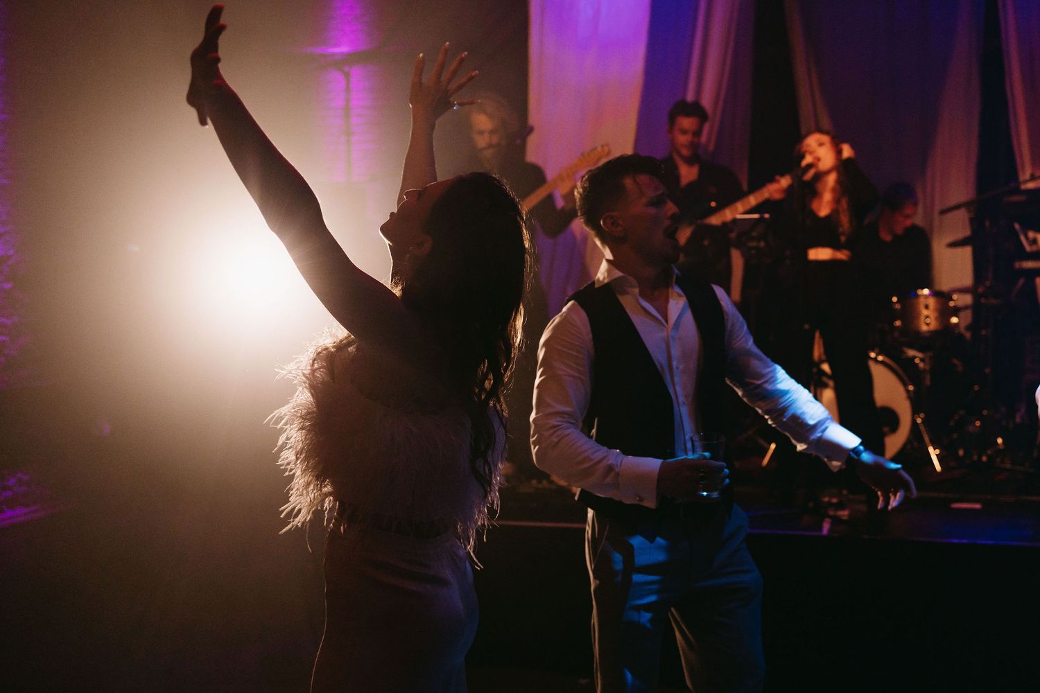 Party guests dance under dramatic purple and white lighting at an evening celebration.
