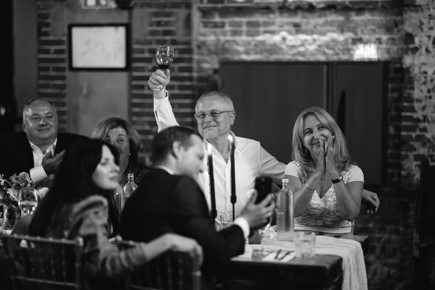 Wedding guests engaged in conversation at tables with exposed brick wall backdrop.