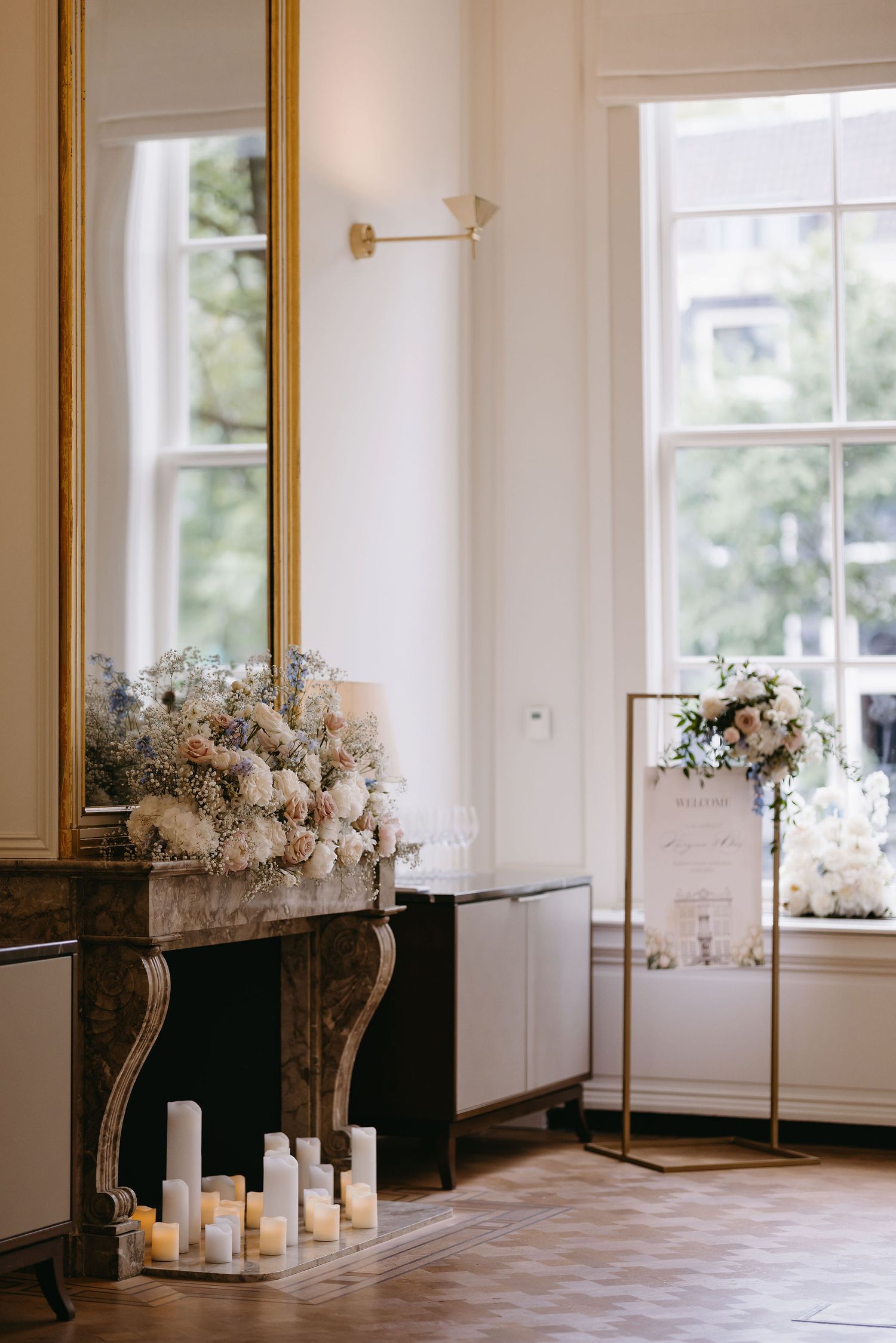 Elegant room interior with gold-framed mirror, white floral arrangements, and candles on the mantle.