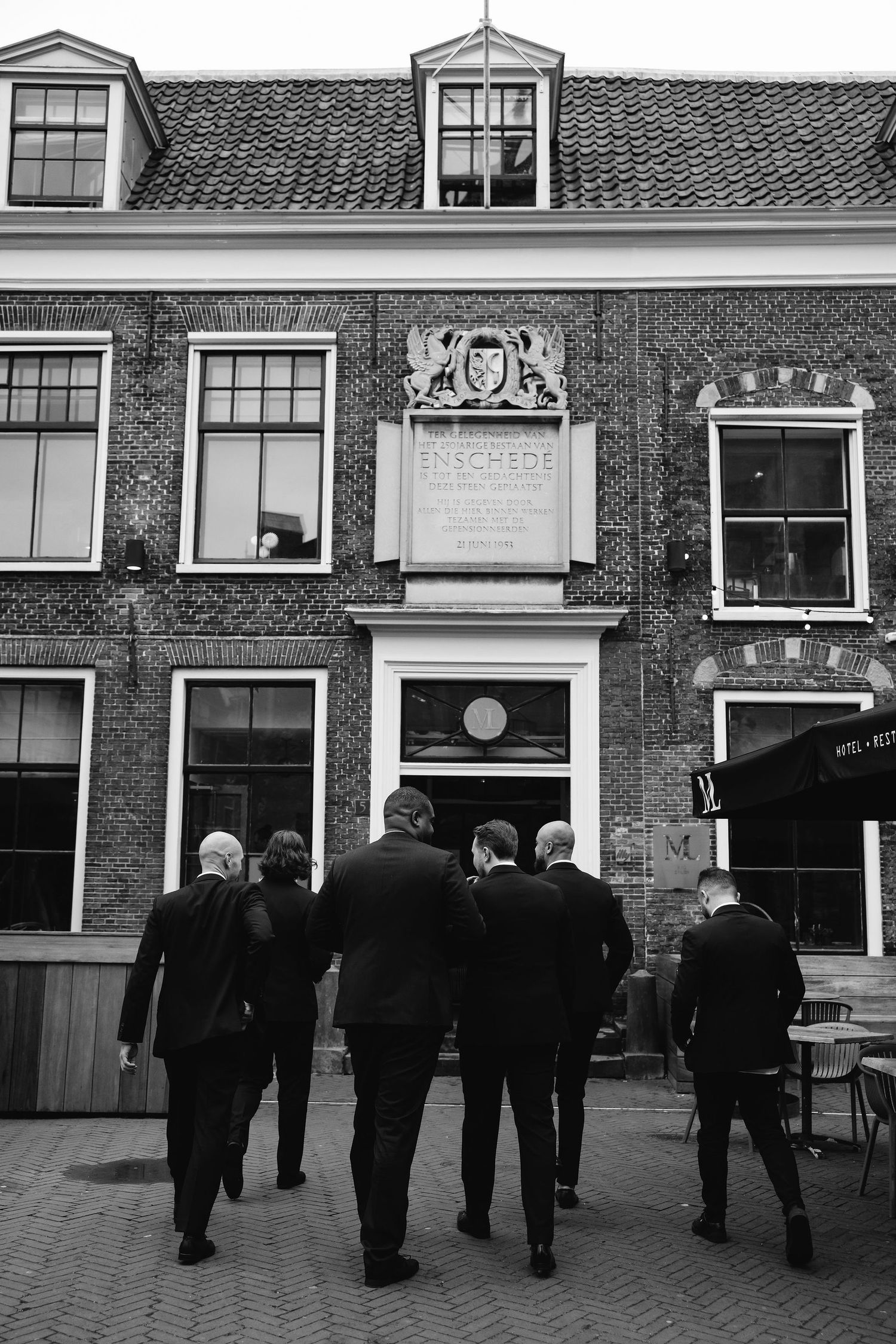 Group of formally dressed people walking towards historic Dutch building entrance.