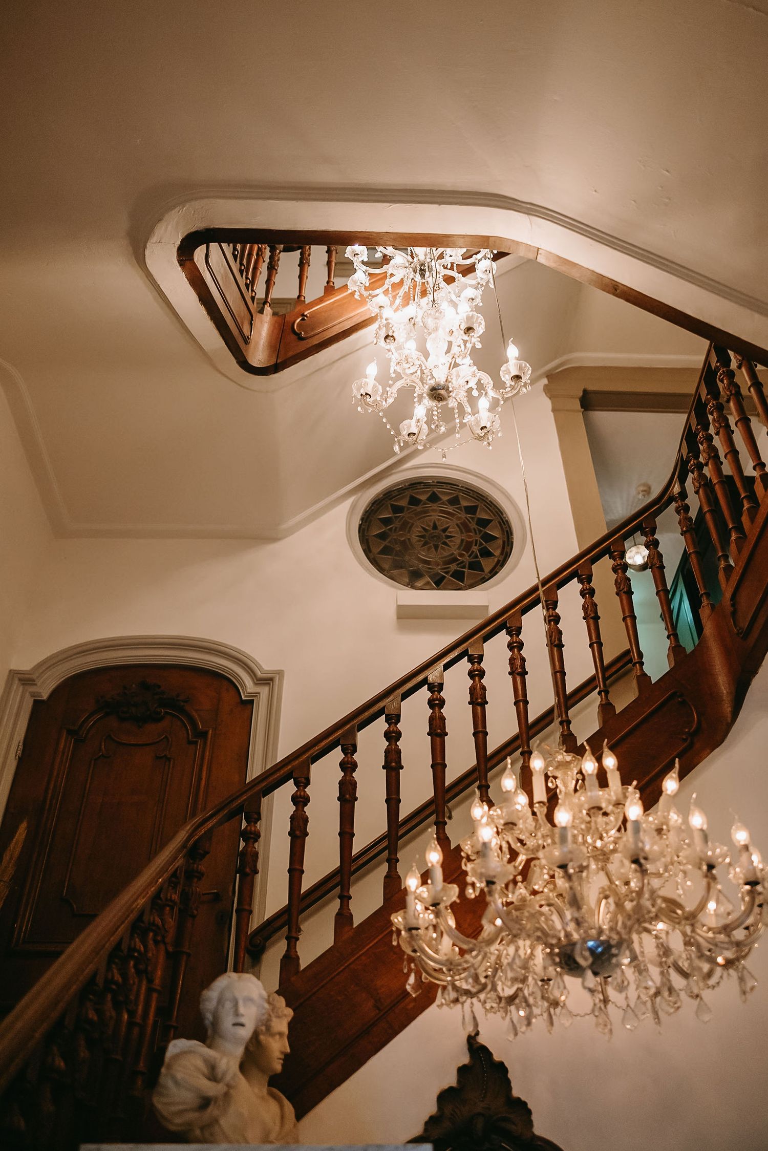 Elegant wooden staircase with crystal chandeliers in a classic interior setting.