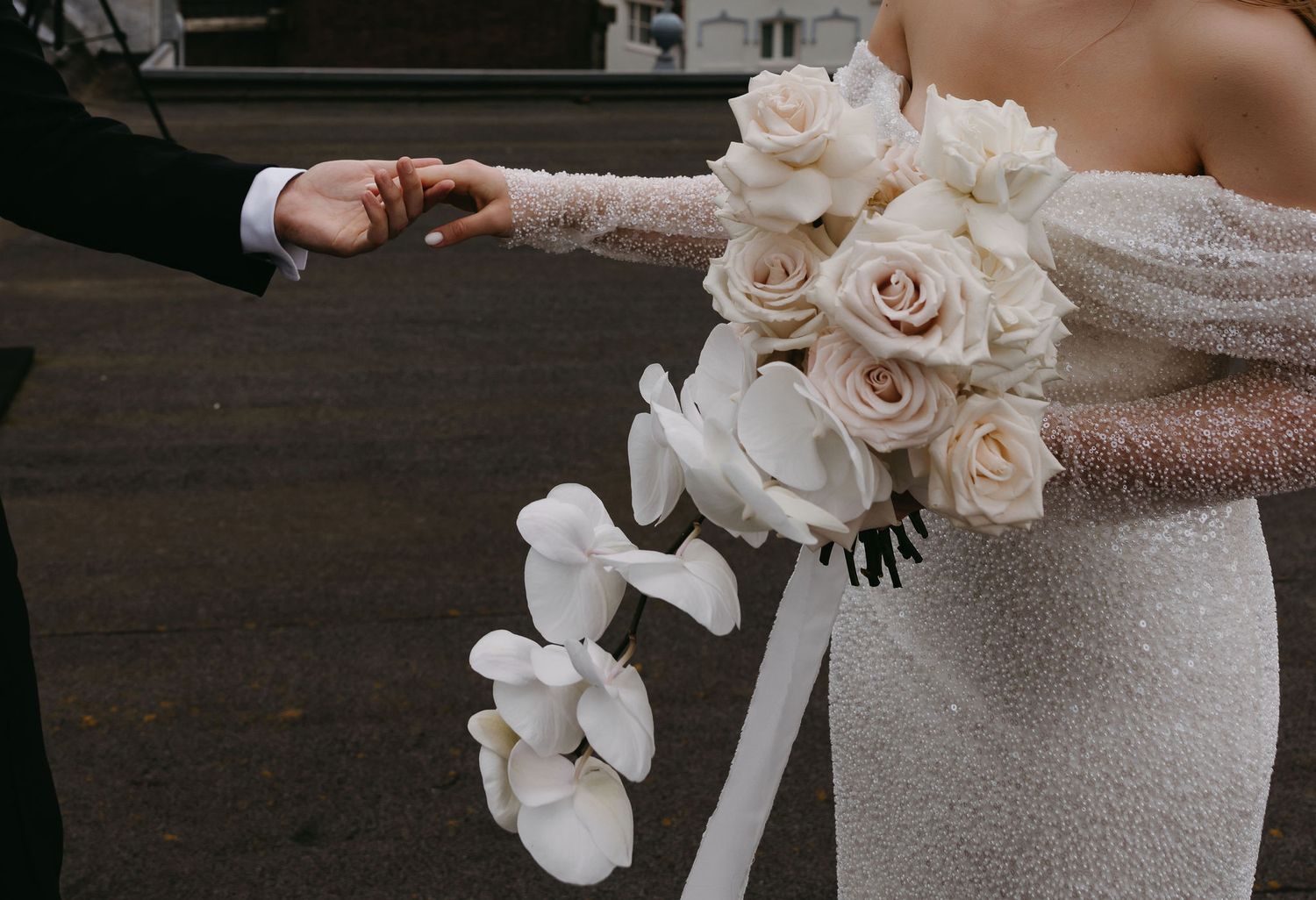 Close-up of bride holding elegant white rose bouquet with ribbon detail.