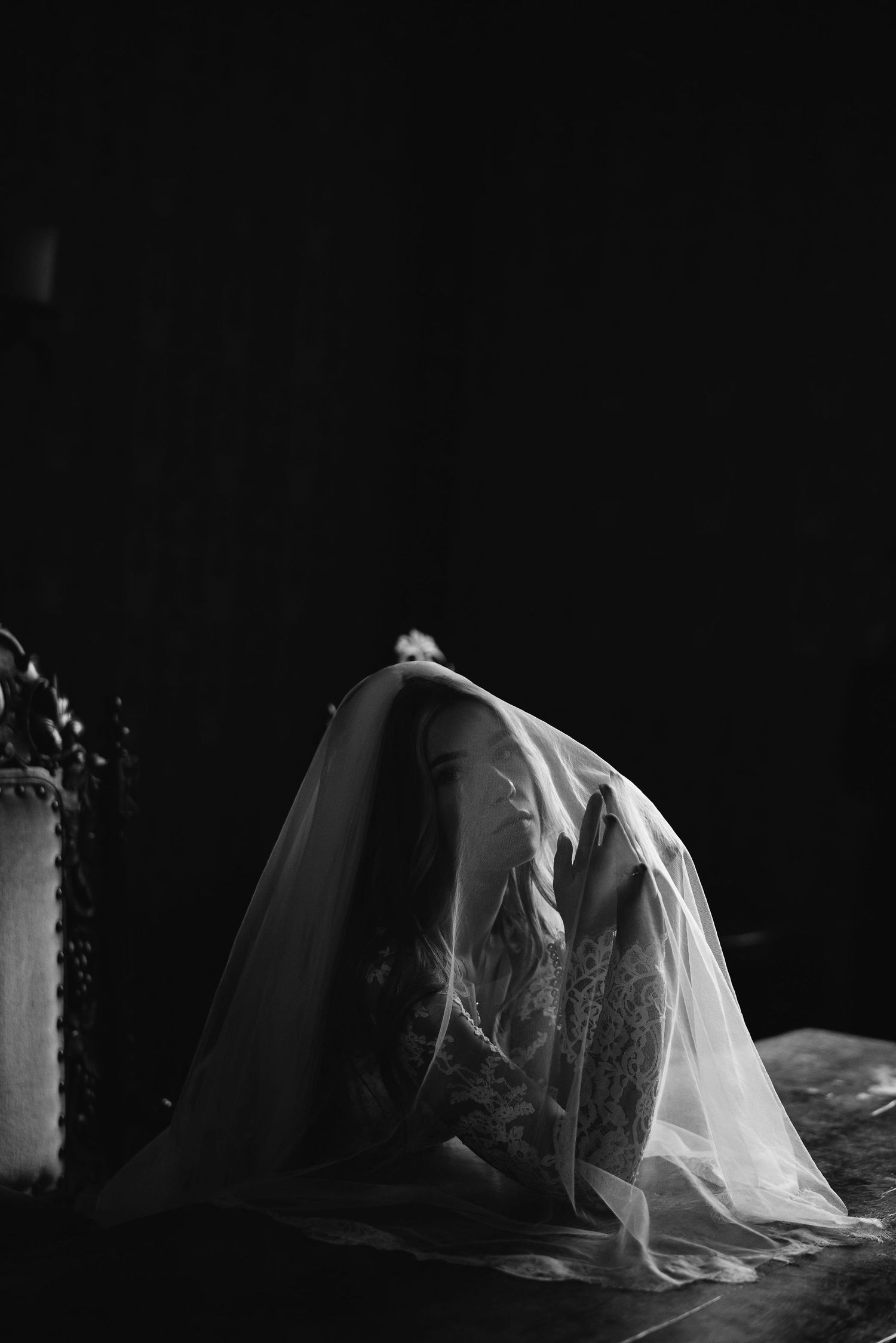 Artistic black and white photo of a bride covered in flowing veil material in dramatic lighting.