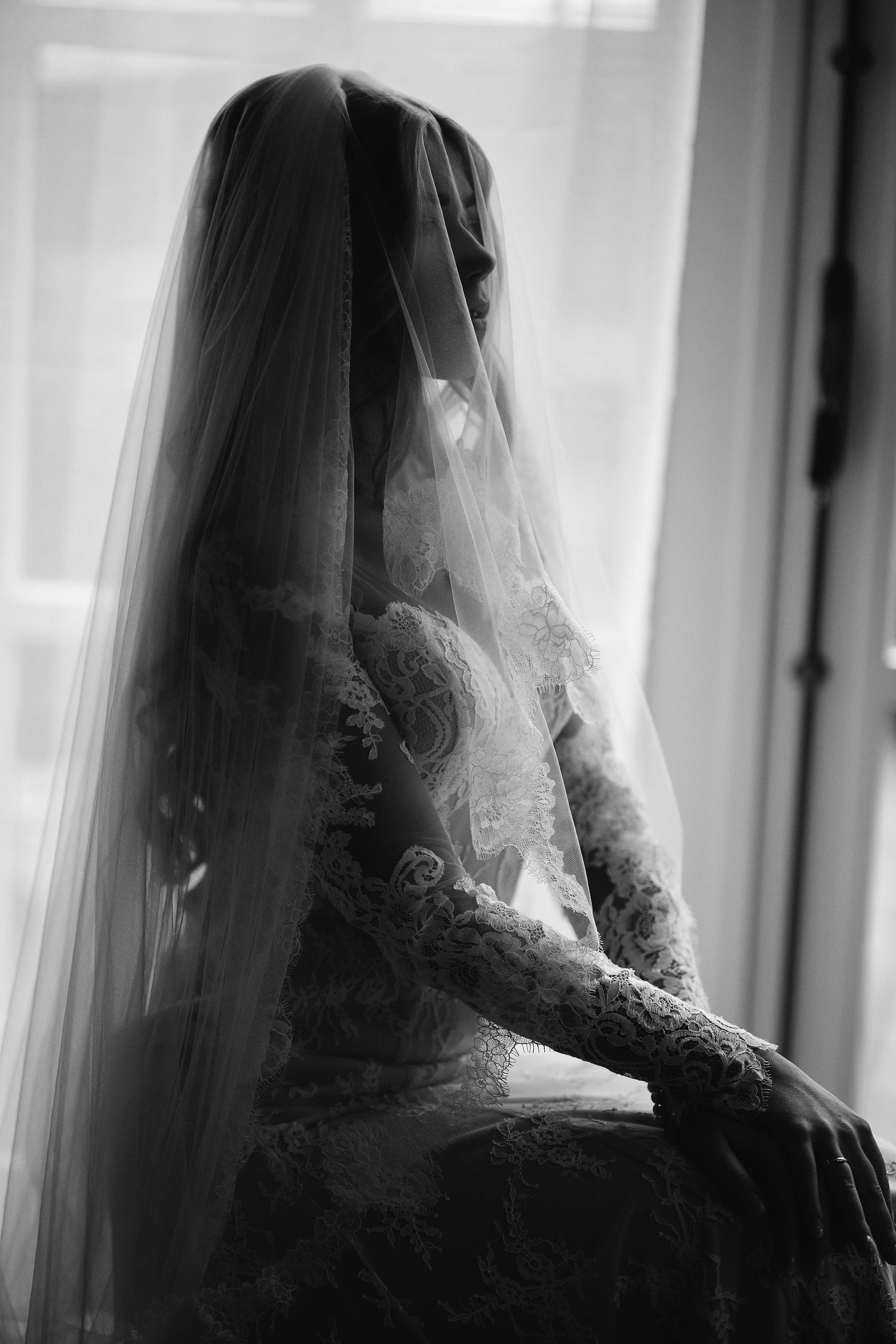 Silhouette of a bride's veil and lace gown details captured in dramatic black and white lighting near a window.
