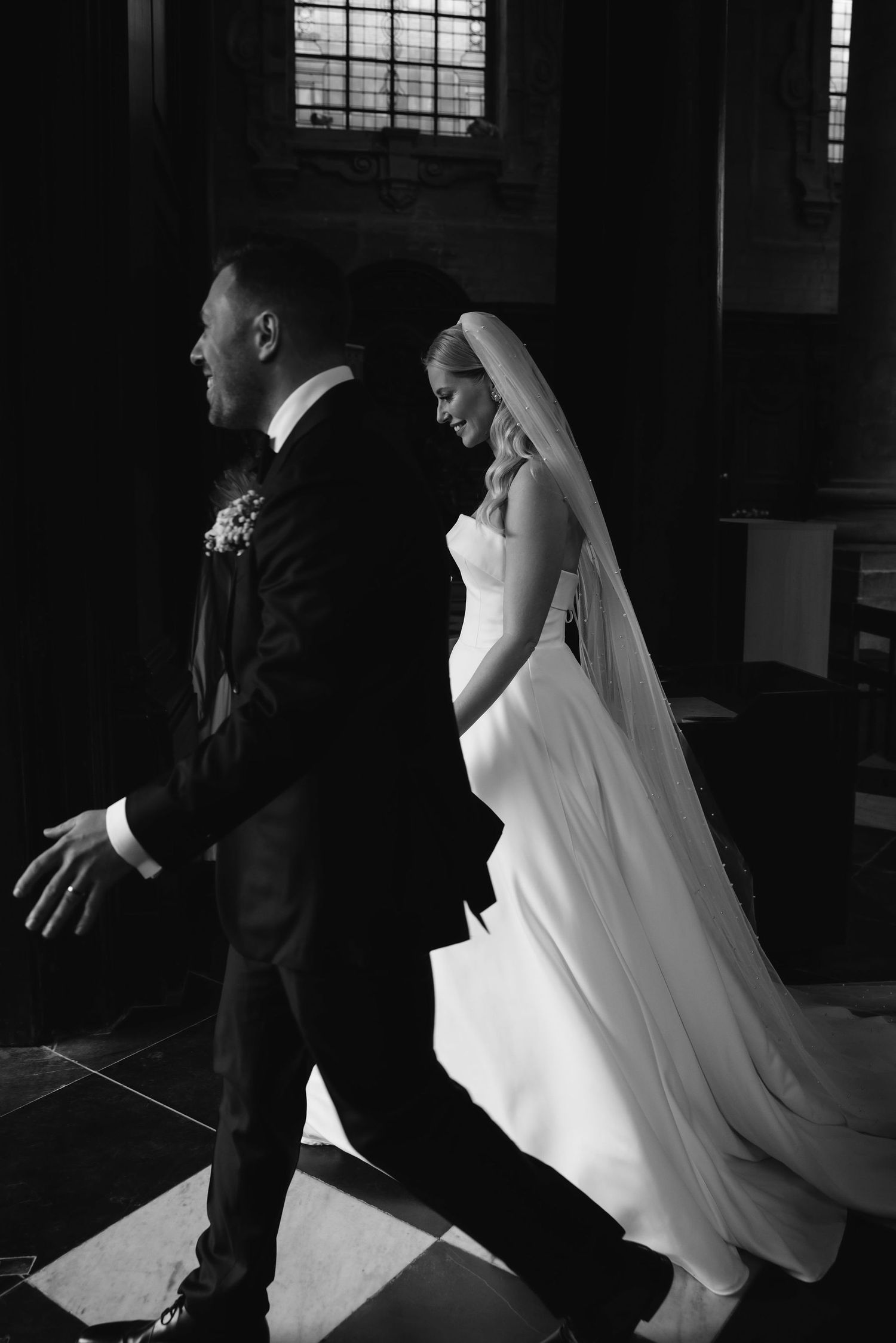 Dramatic black and white photo of a wedding couple walking in profile through a historic building.
