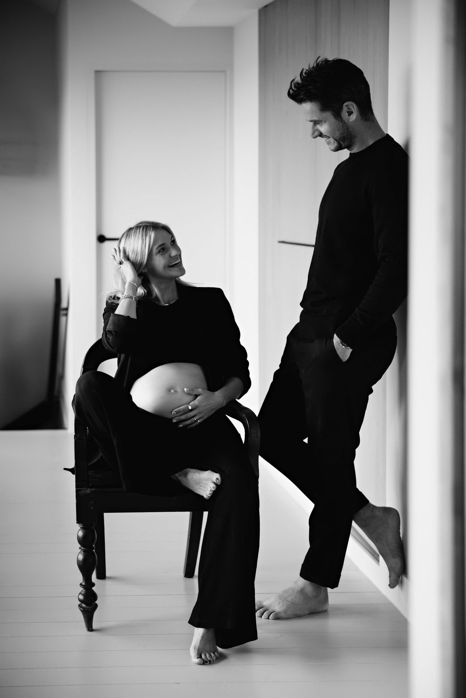 Black and white maternity photo with two people in casual attire having an intimate moment.