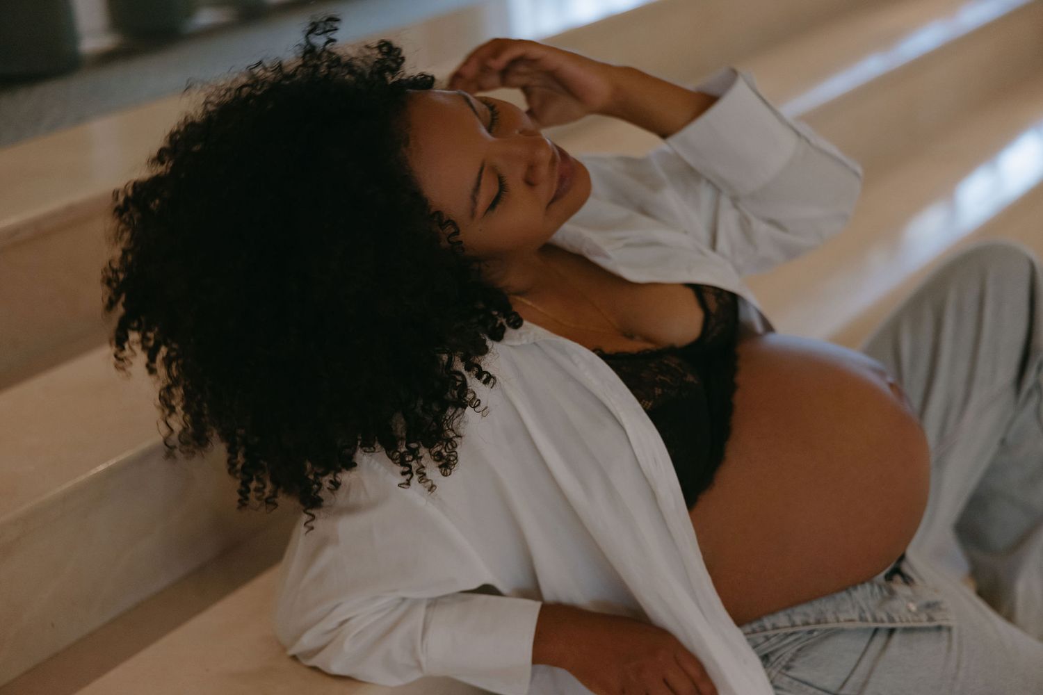 Candid lifestyle photos of woman lounging on sunlit floor in bright white sweater and jeans.