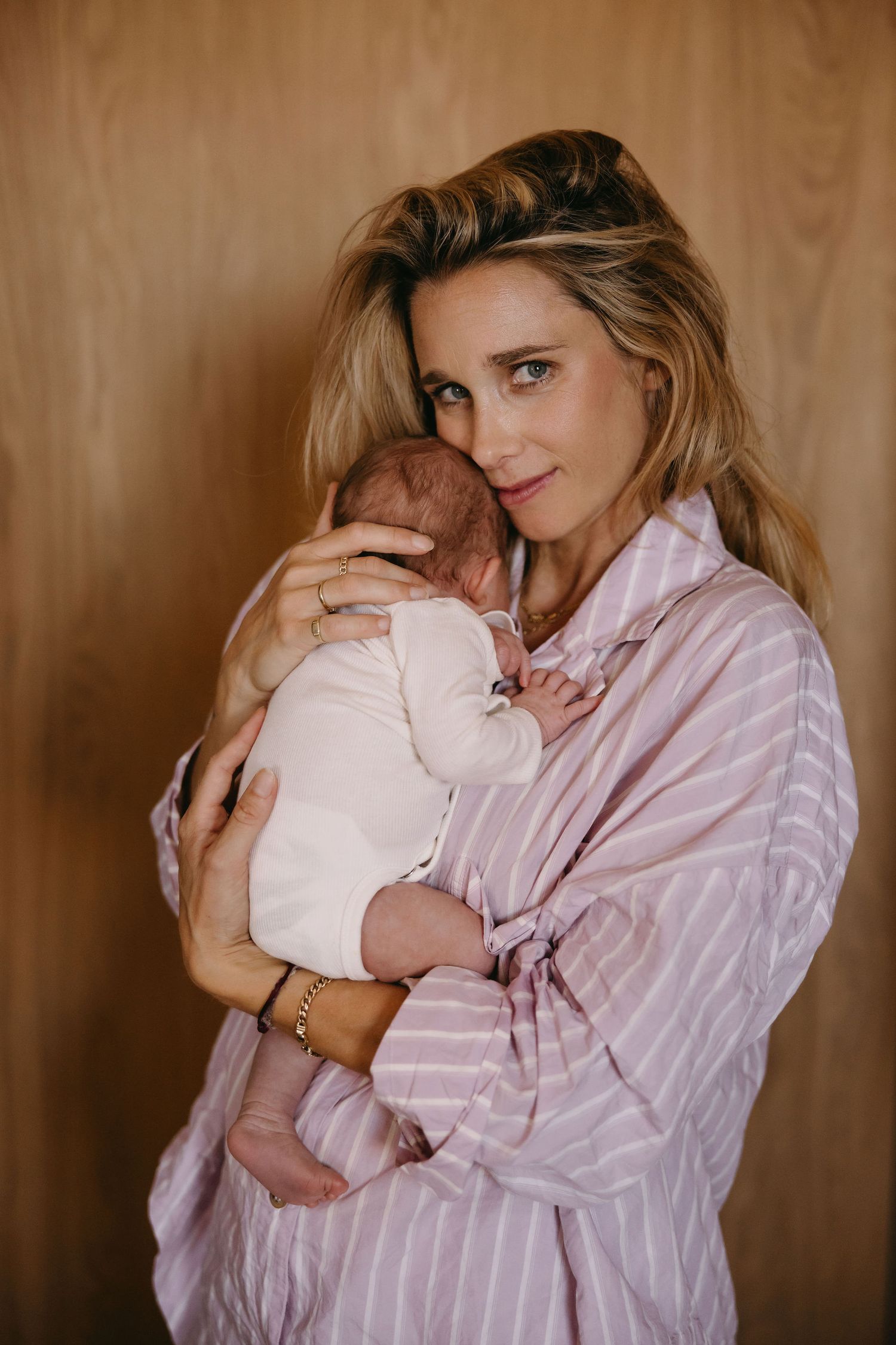 A tender moment between a parent wearing a pink striped shirt and their newborn baby against a wooden background.
