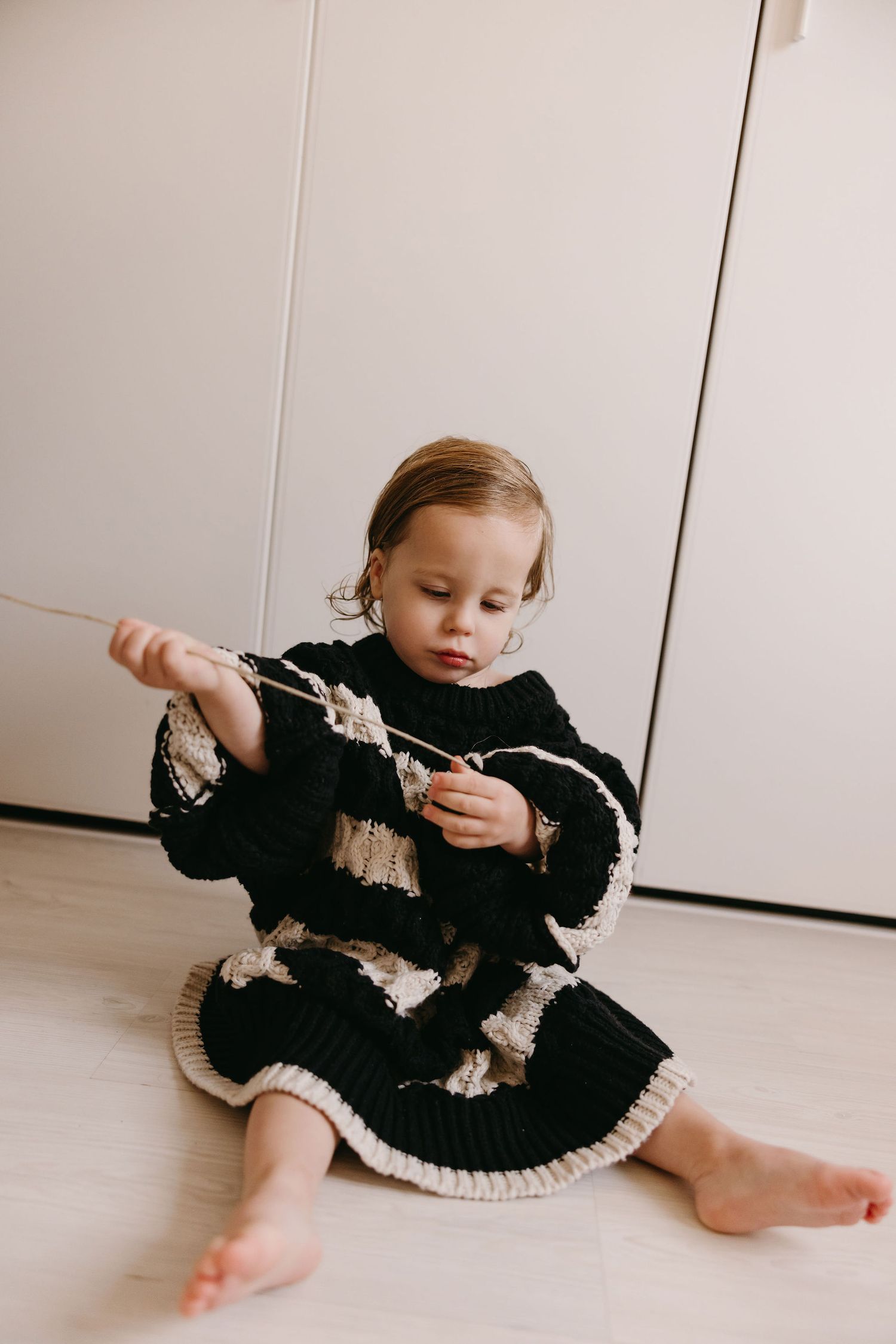 Small child in black and white knit dress plays with toys on floor.