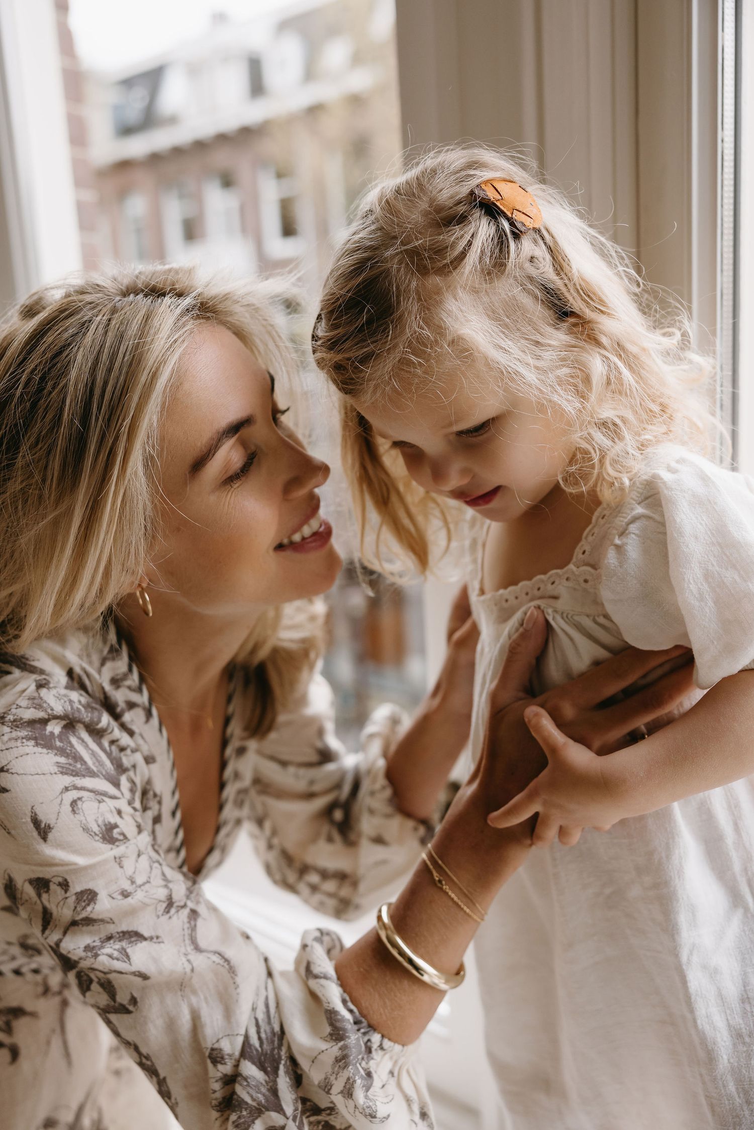 Tender mother-daughter moments captured in soft natural window light.