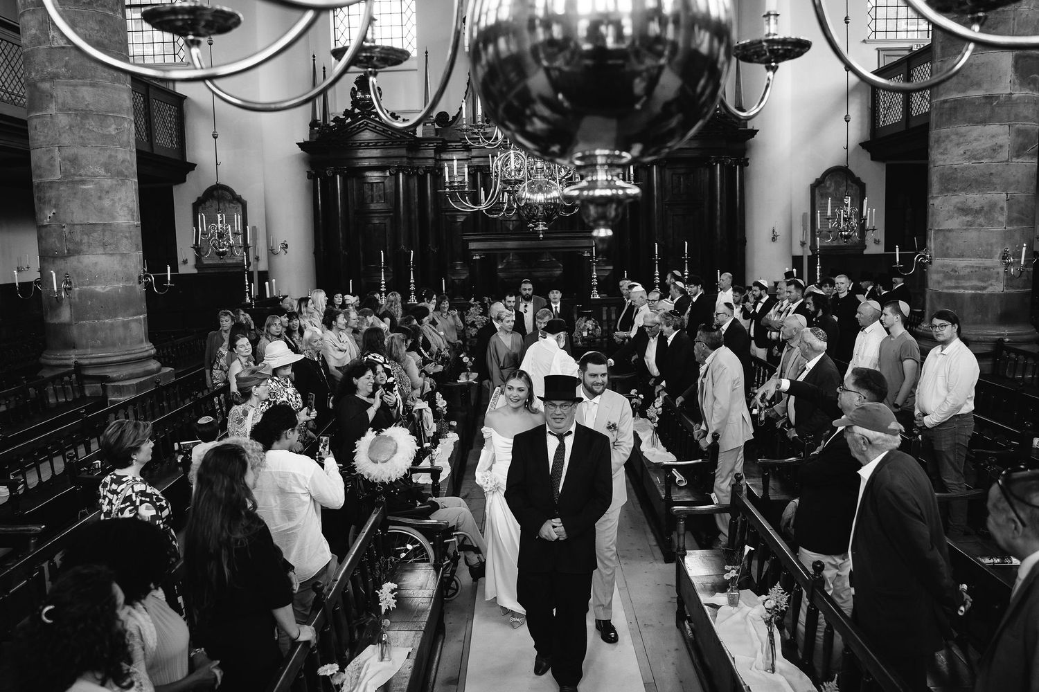 Wedding guests dancing and celebrating in a dimly lit church or venue space.