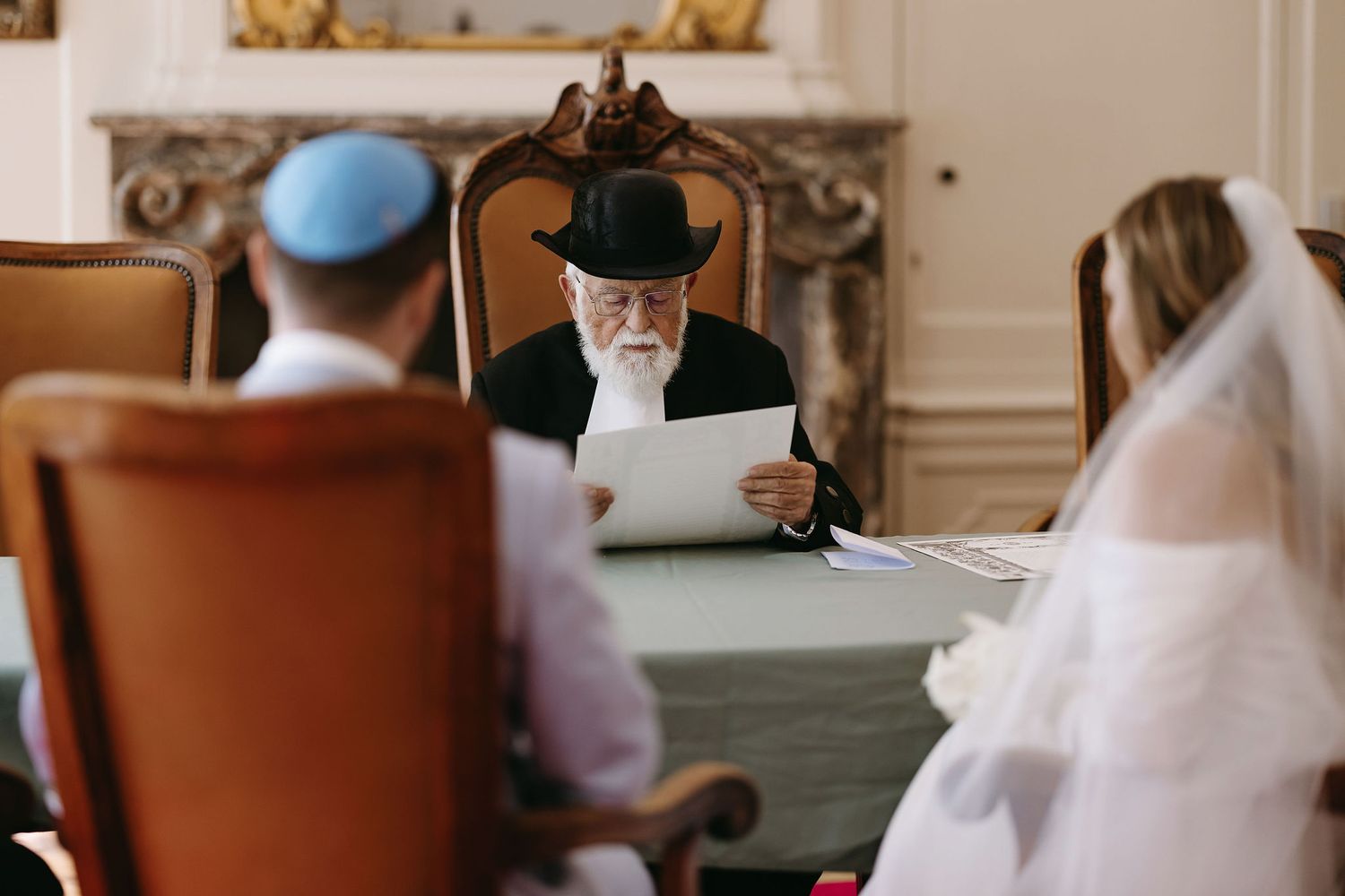 Religious wedding ceremony taking place in an ornate room with participants seated at a formal table.
