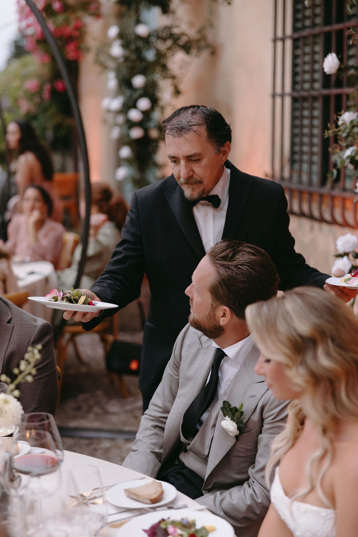 A waiter serves guests at an elegant outdoor wedding reception under string lights.