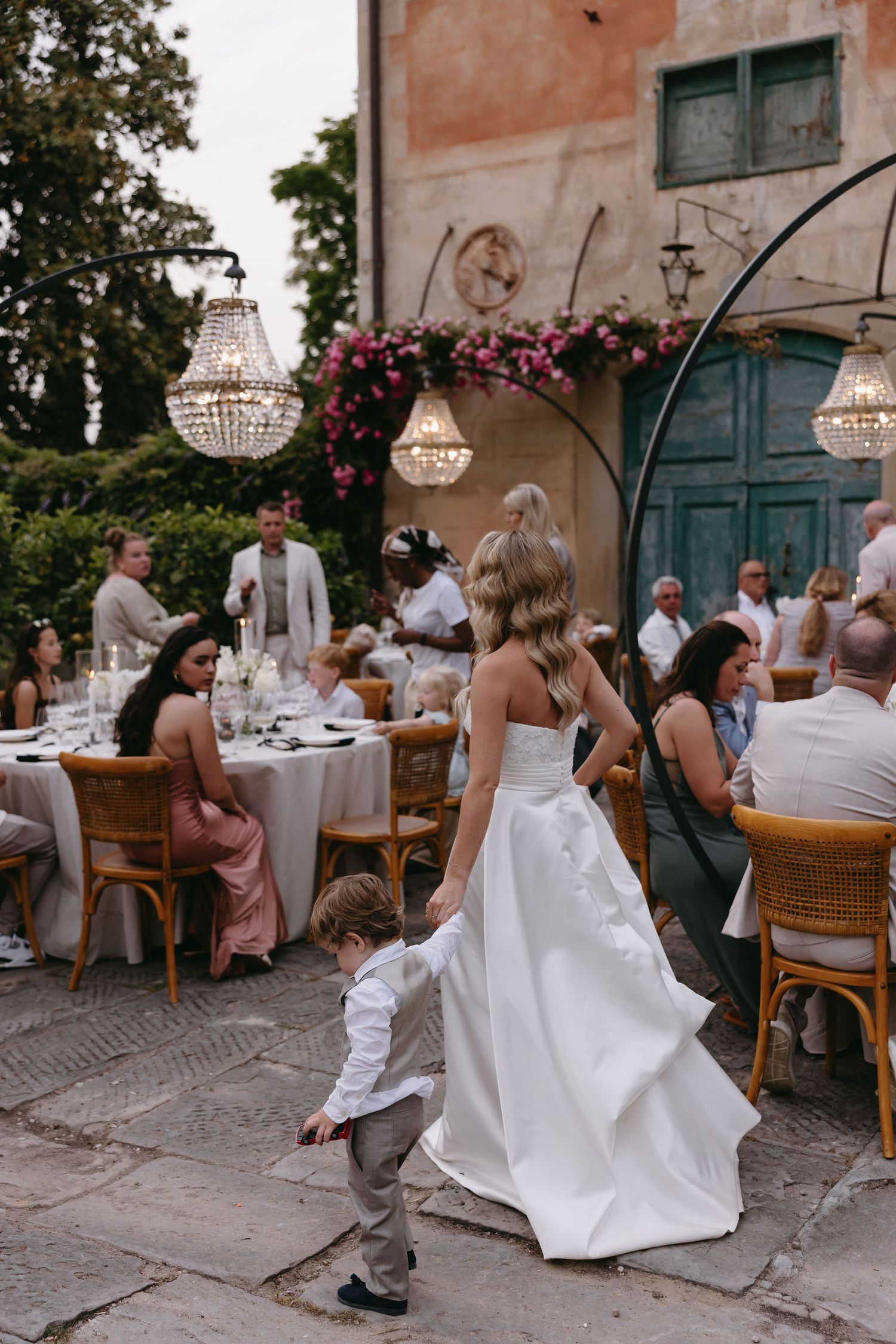Elegant outdoor wedding reception with crystal chandeliers and guests dining at decorated tables.