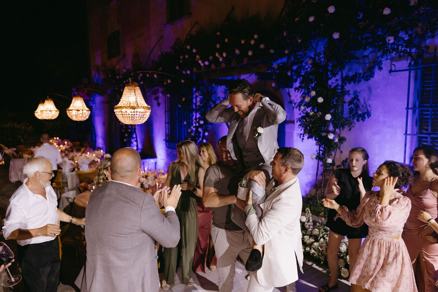 Wedding reception dance floor filled with guests under purple lighting and hanging lanterns.