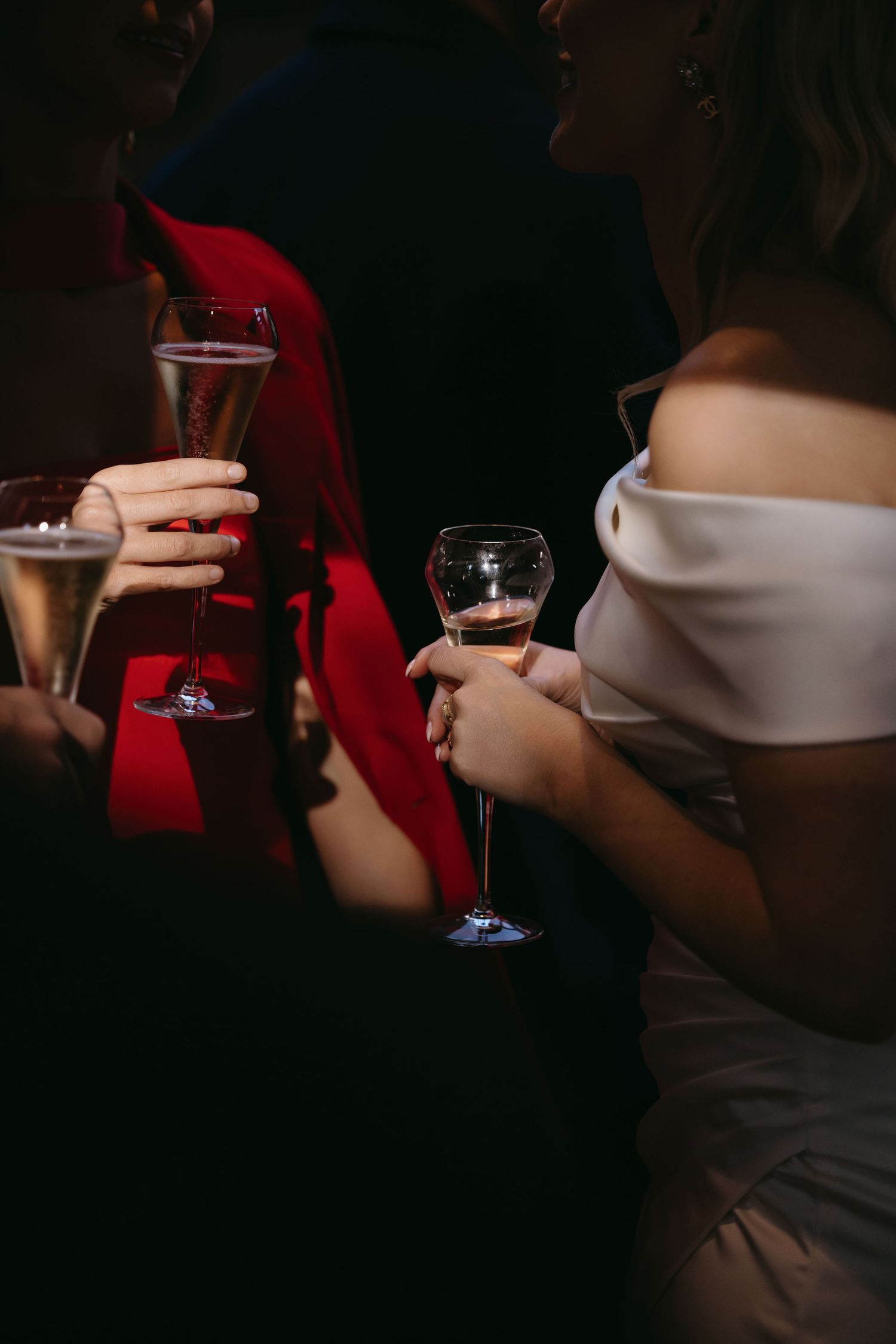 Close-up of party guests holding champagne glasses in a dimly lit setting.